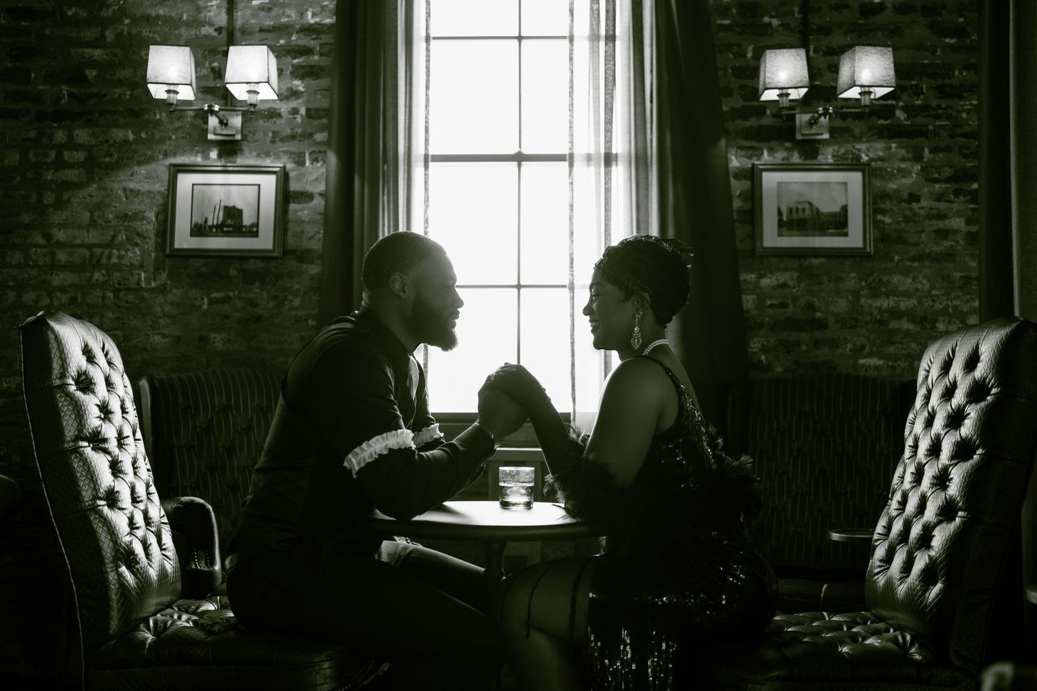 A silhouetted couple sharing an intimate moment at a table by a window.
