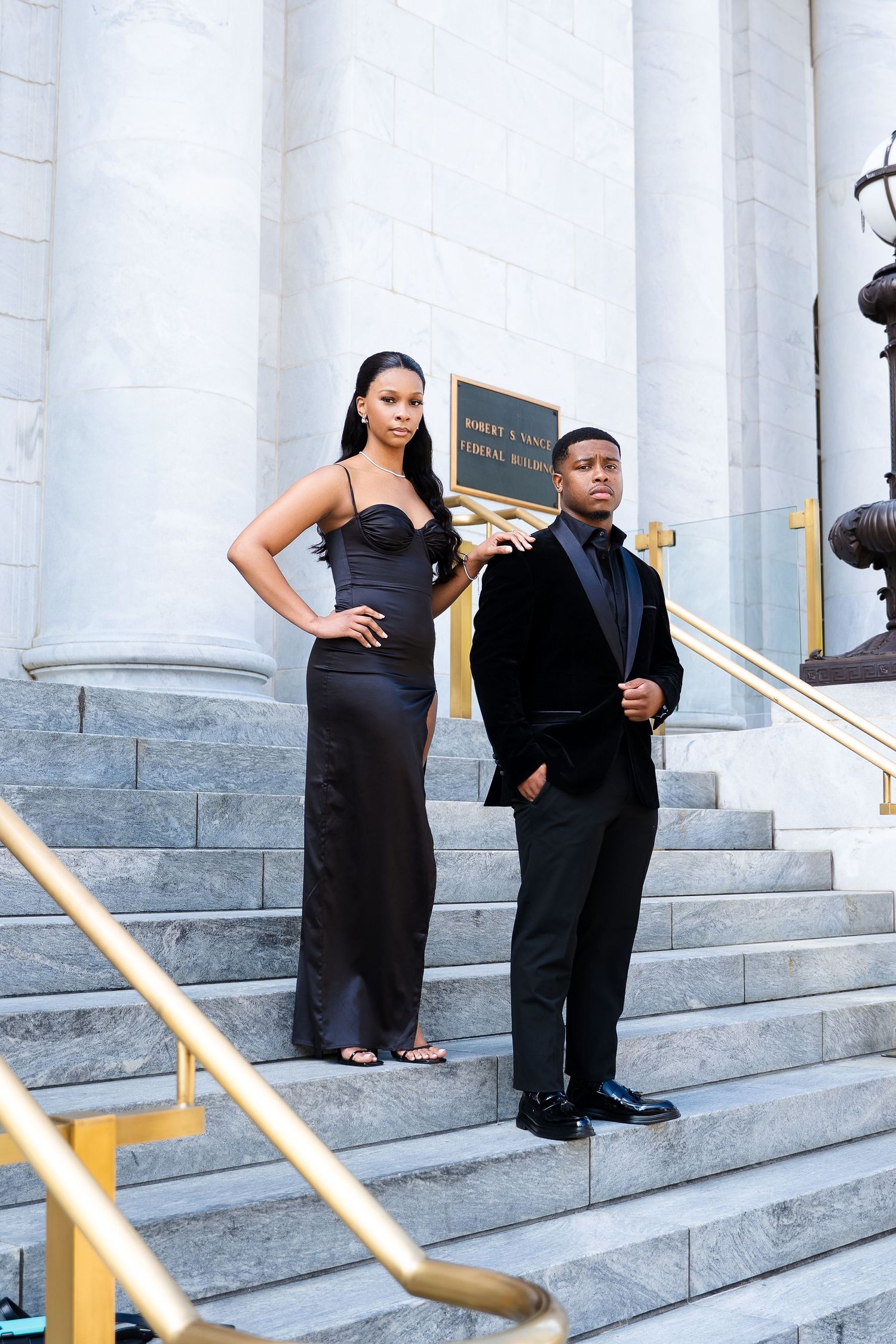 A formal couple posing on white stone steps in elegant evening attire.