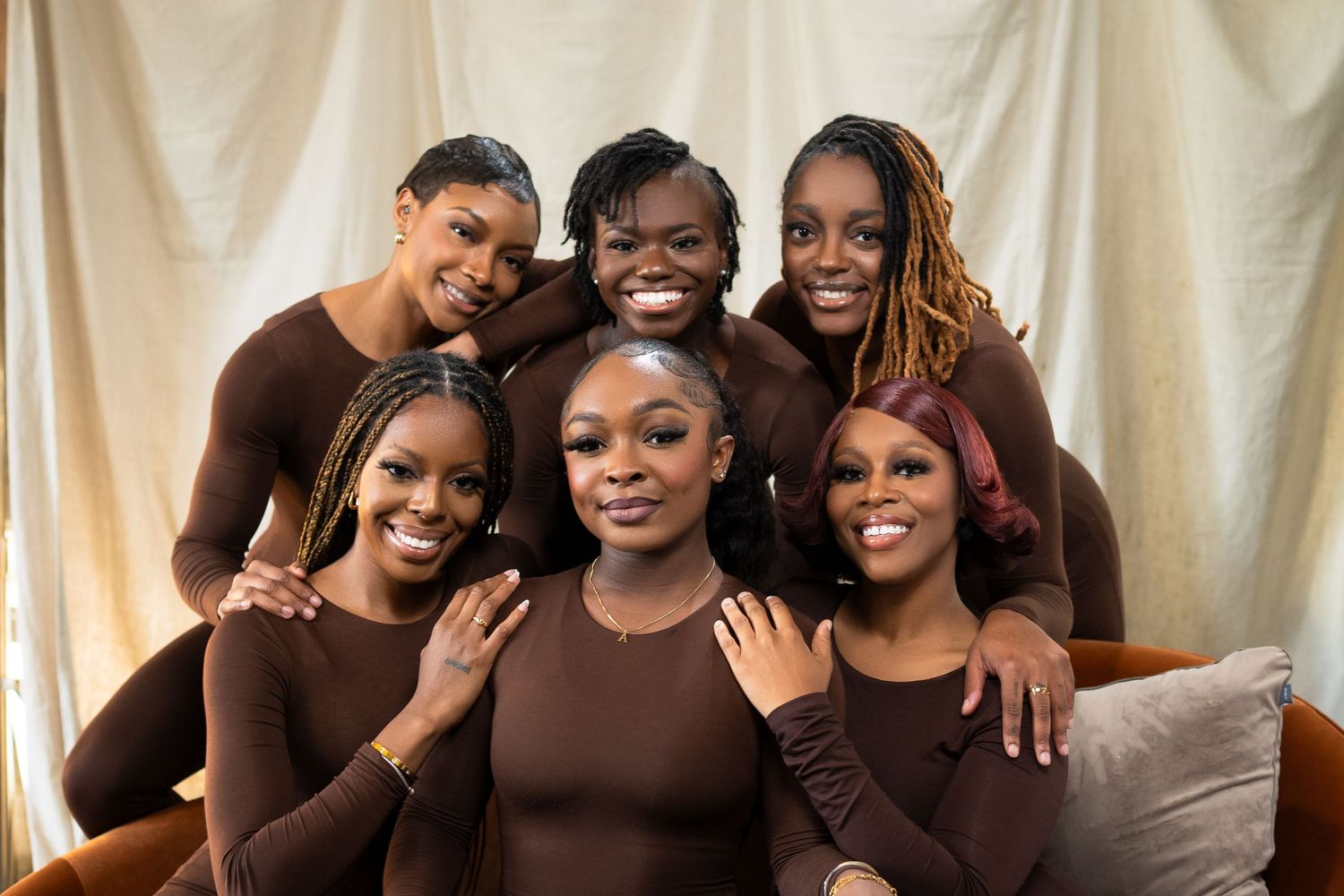 Group photo of six people in matching brown outfits against light backdrop.