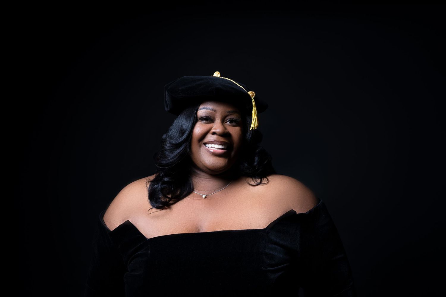Dramatic portrait of graduate in black gown against dark background.