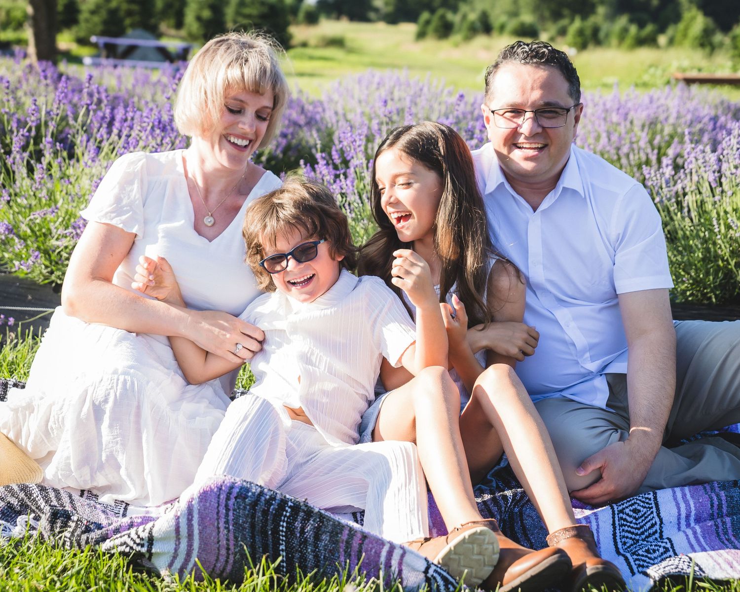 A family sits together on a blanket in a blooming lavender field on a sunny summer day.
