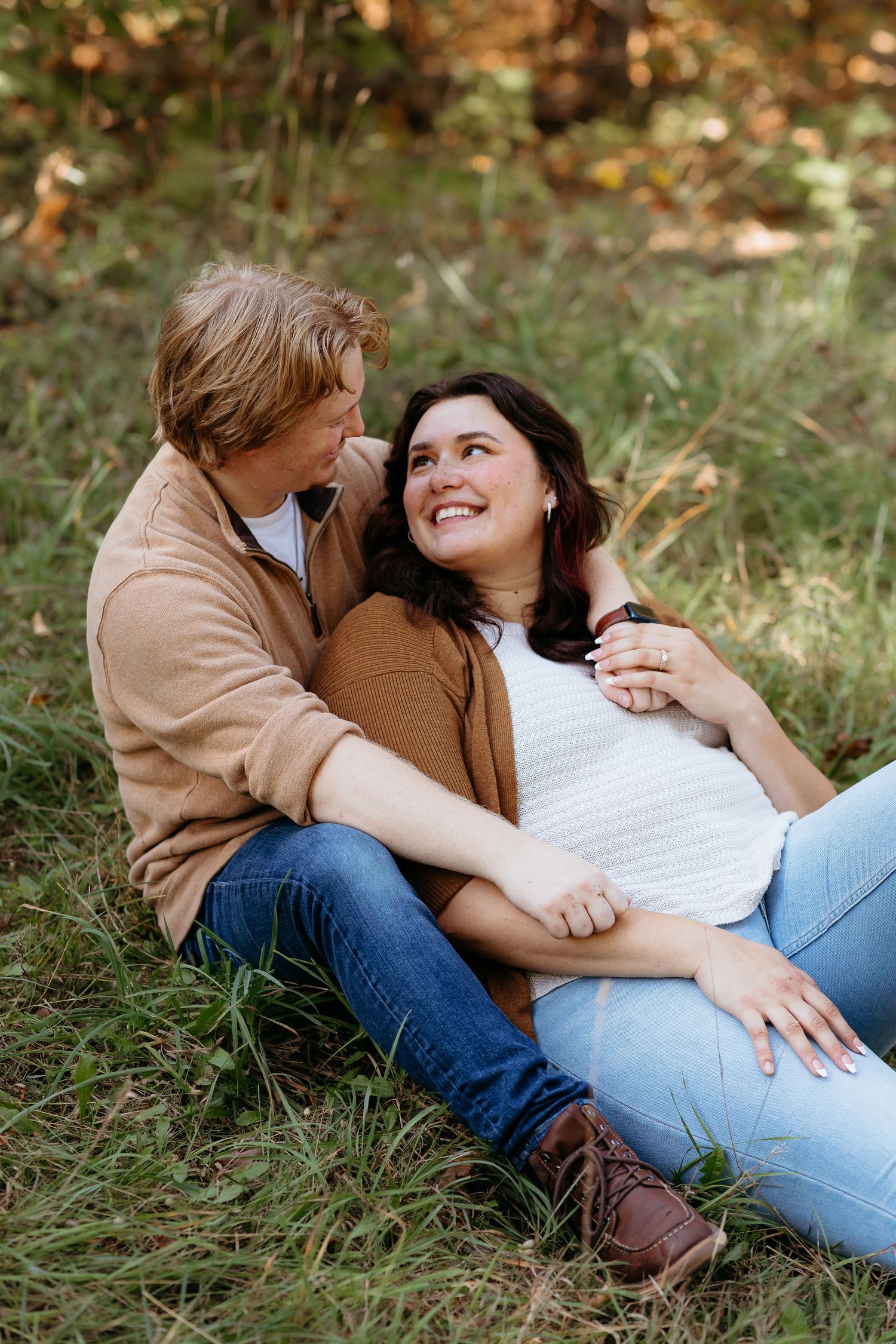 A couple in casual autumn attire shares intimate moments while relaxing together on grass in a romantic outdoor setting.