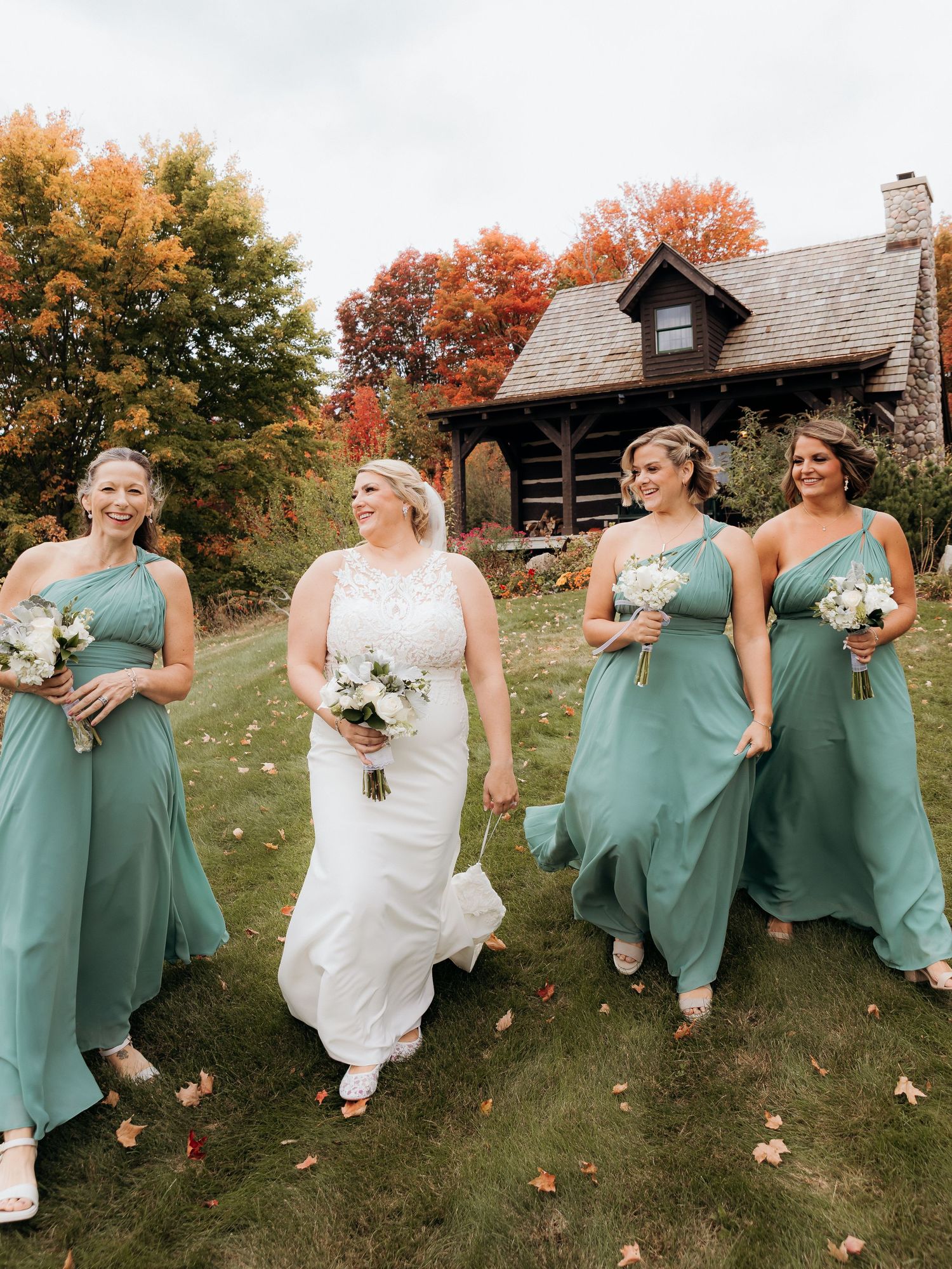 Wedding party in seafoam green dresses walking across a grassy hill with fall colors.