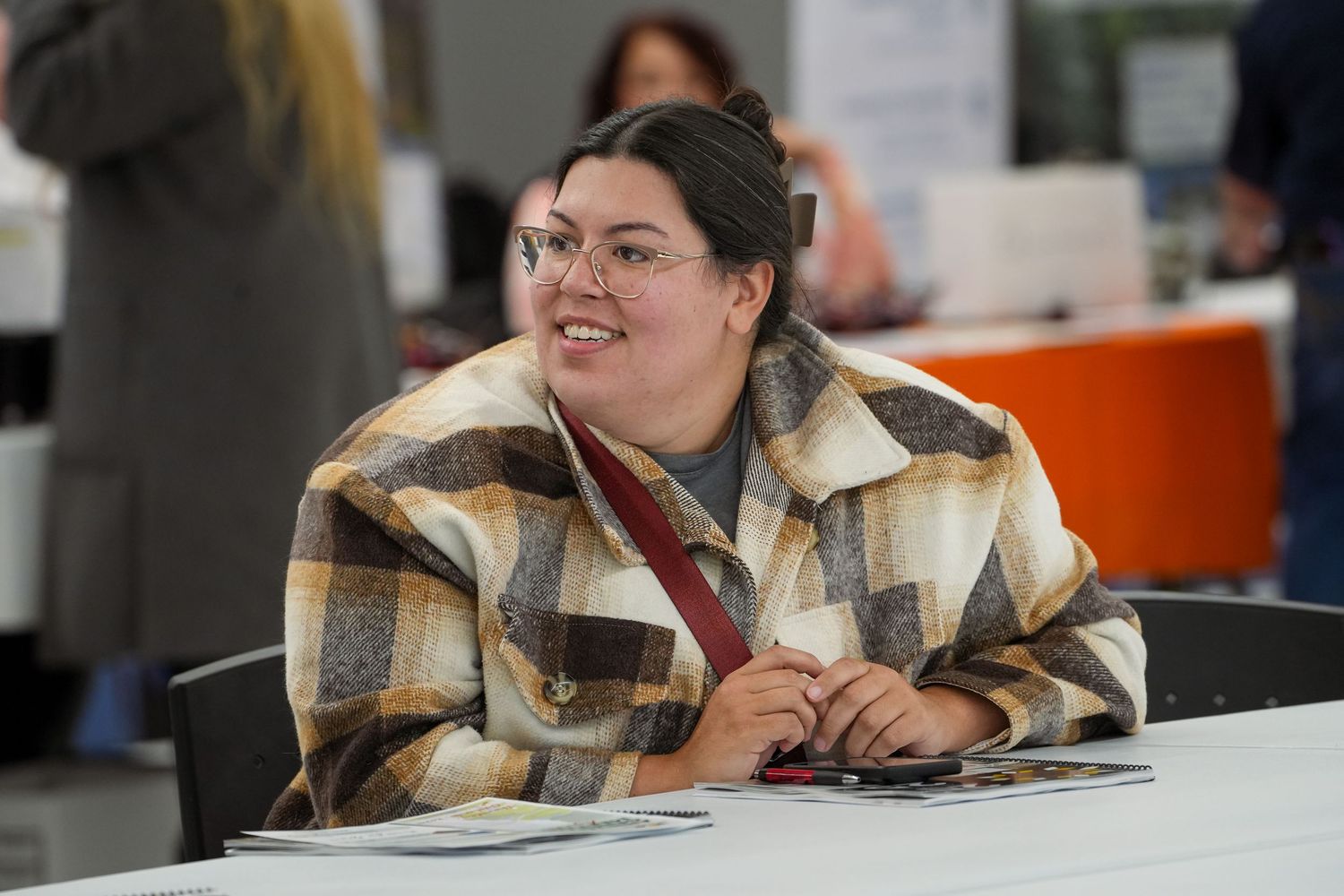 People seated at tables during indoor event wearing plaid shirts.