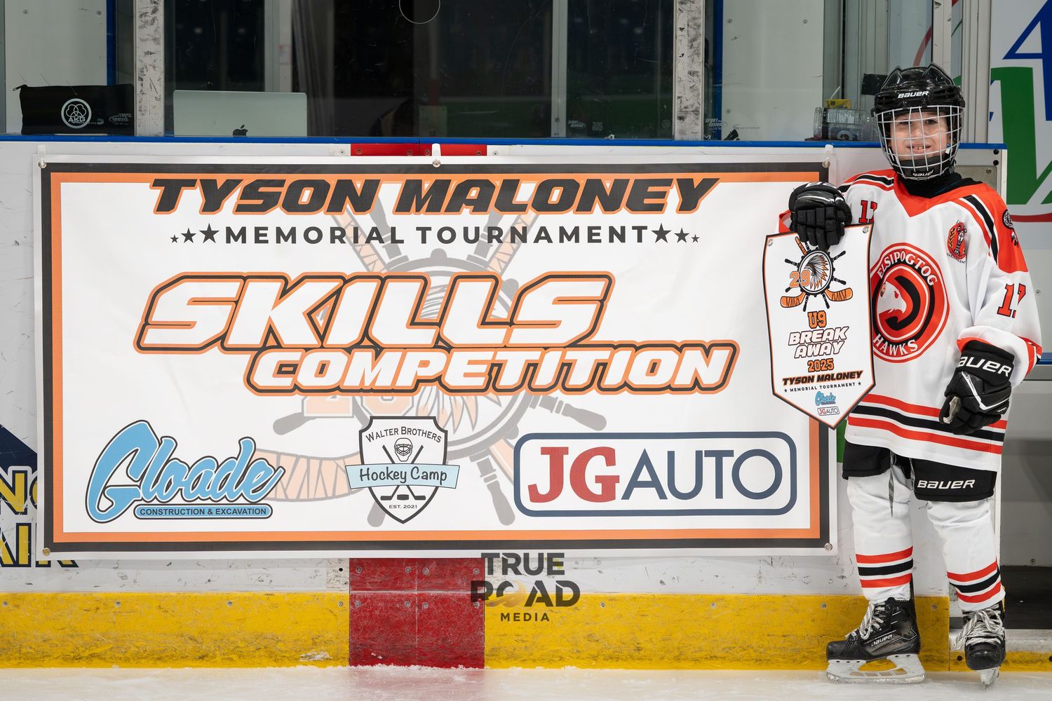 Hockey player stands by Tyson Maloney Skills Competition banner at ice rink.
