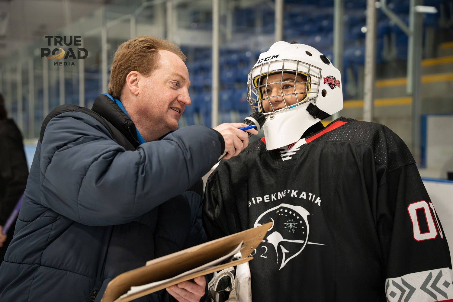 Hockey coaches and players interacting at the boards during practice session.