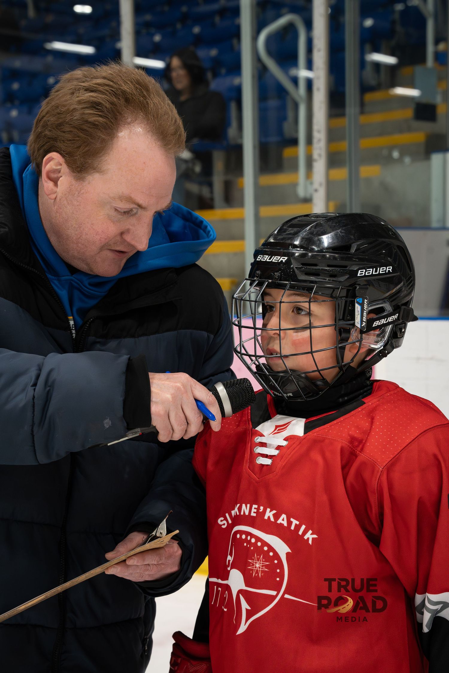 Coach adjusting hockey equipment on a player wearing a red jersey during practice.