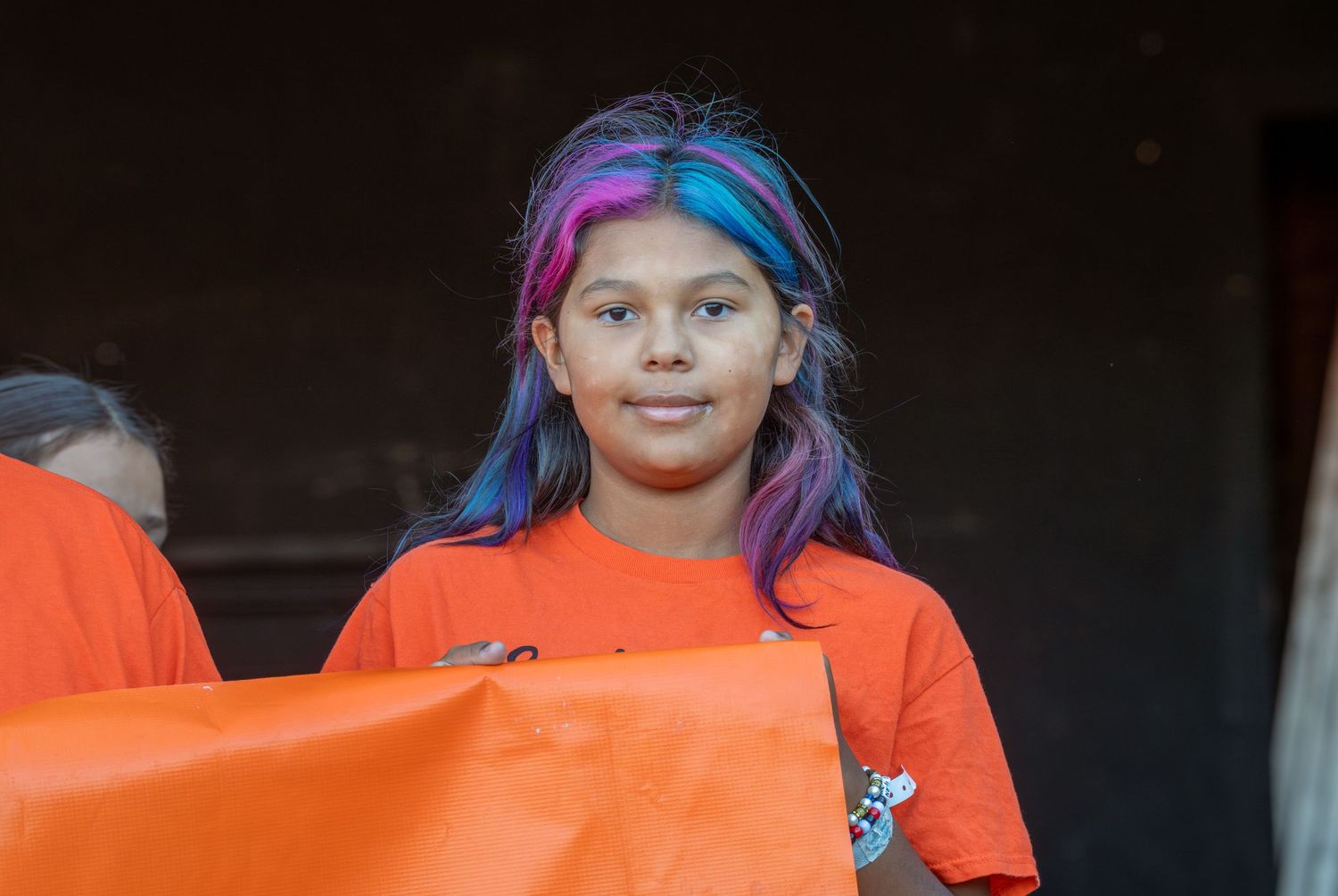 A group of children wearing bright orange safety vests stand together.