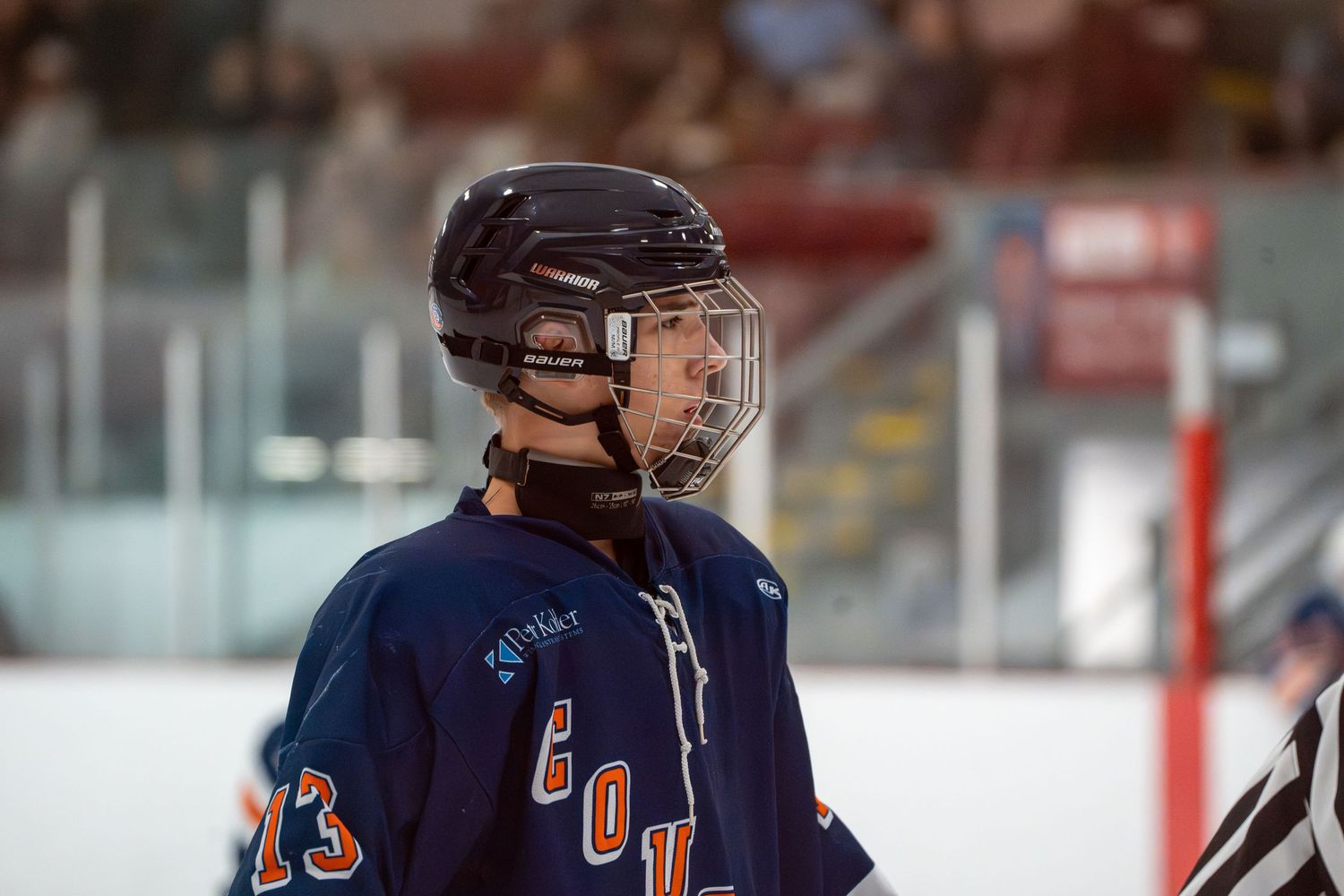 Hockey player in navy blue jersey and helmet looking to the side during a game.