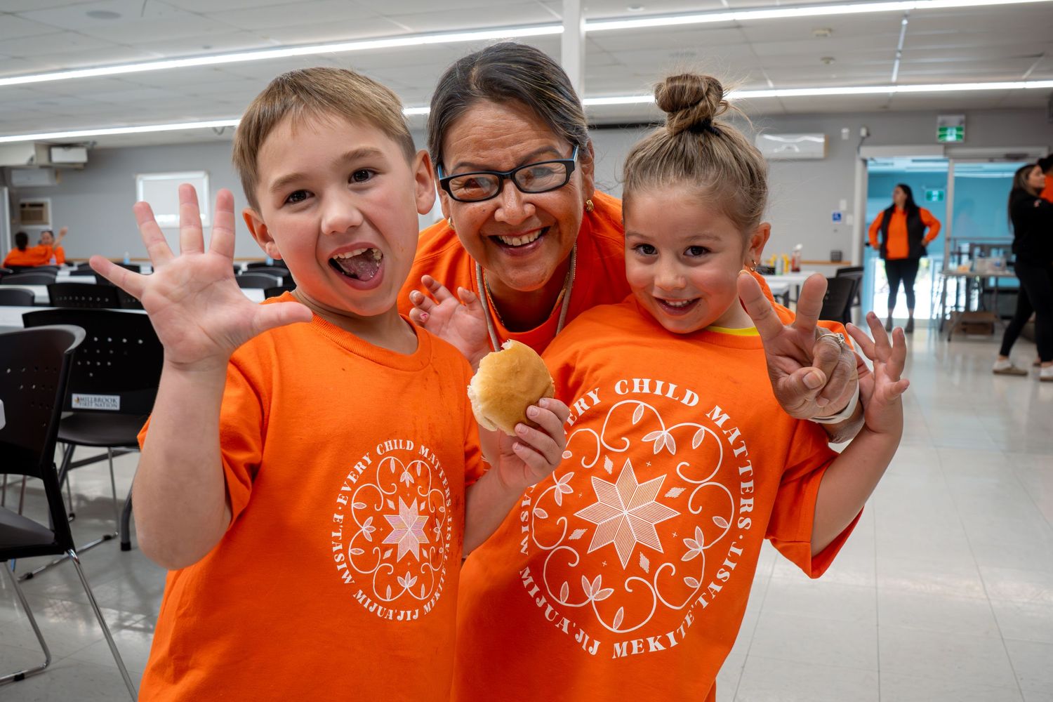 Enthusiastic group wearing matching bright orange t-shirts gathered indoors showing excitement and team spirit.