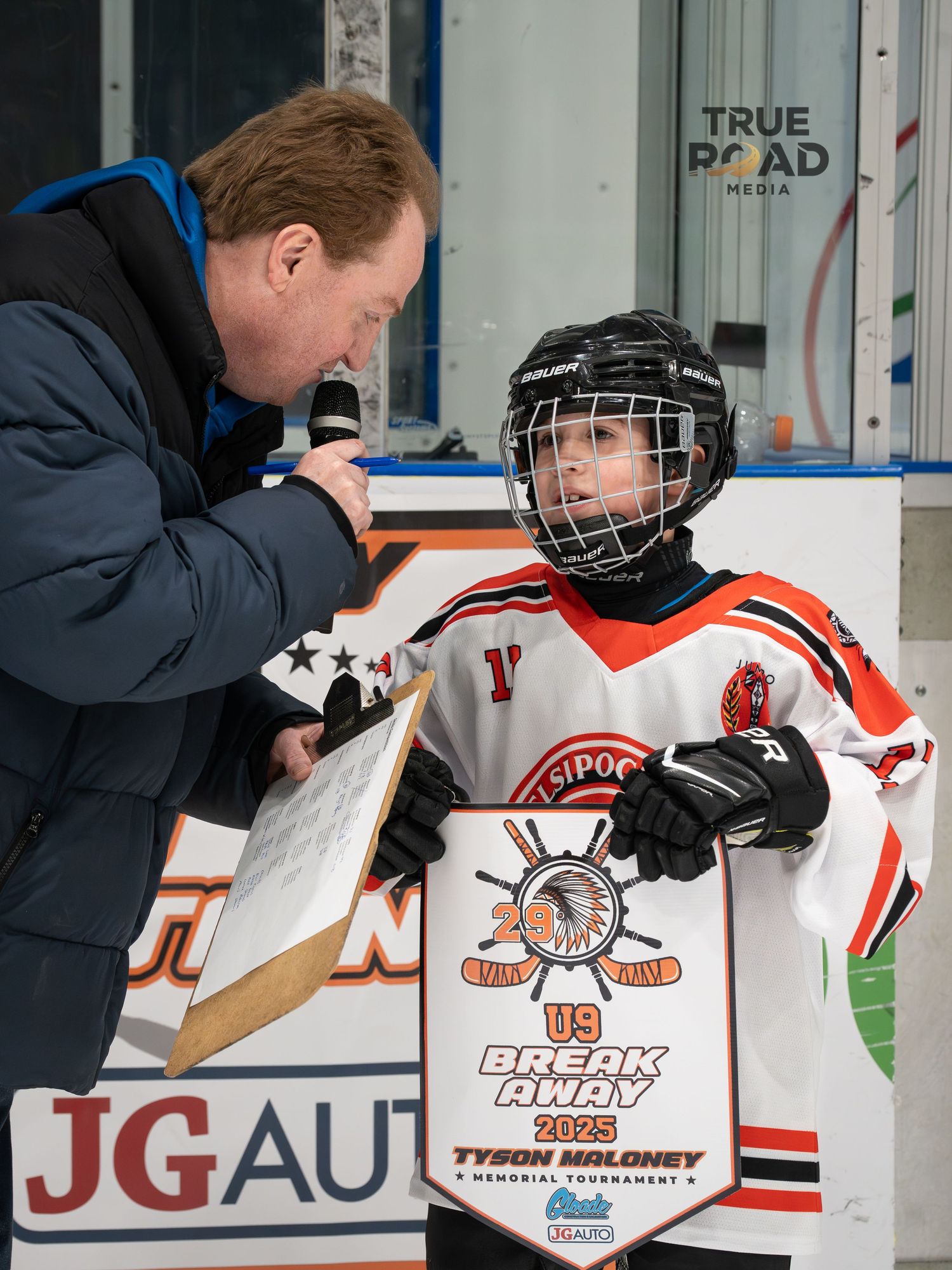 Sports announcer conducts interview with youth hockey player in orange jersey during game.