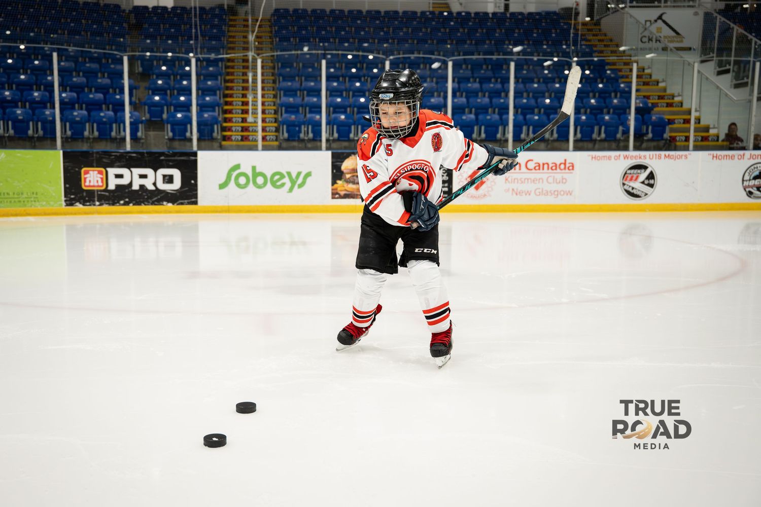 Hockey player in red and white jersey practices puck handling drills on ice.