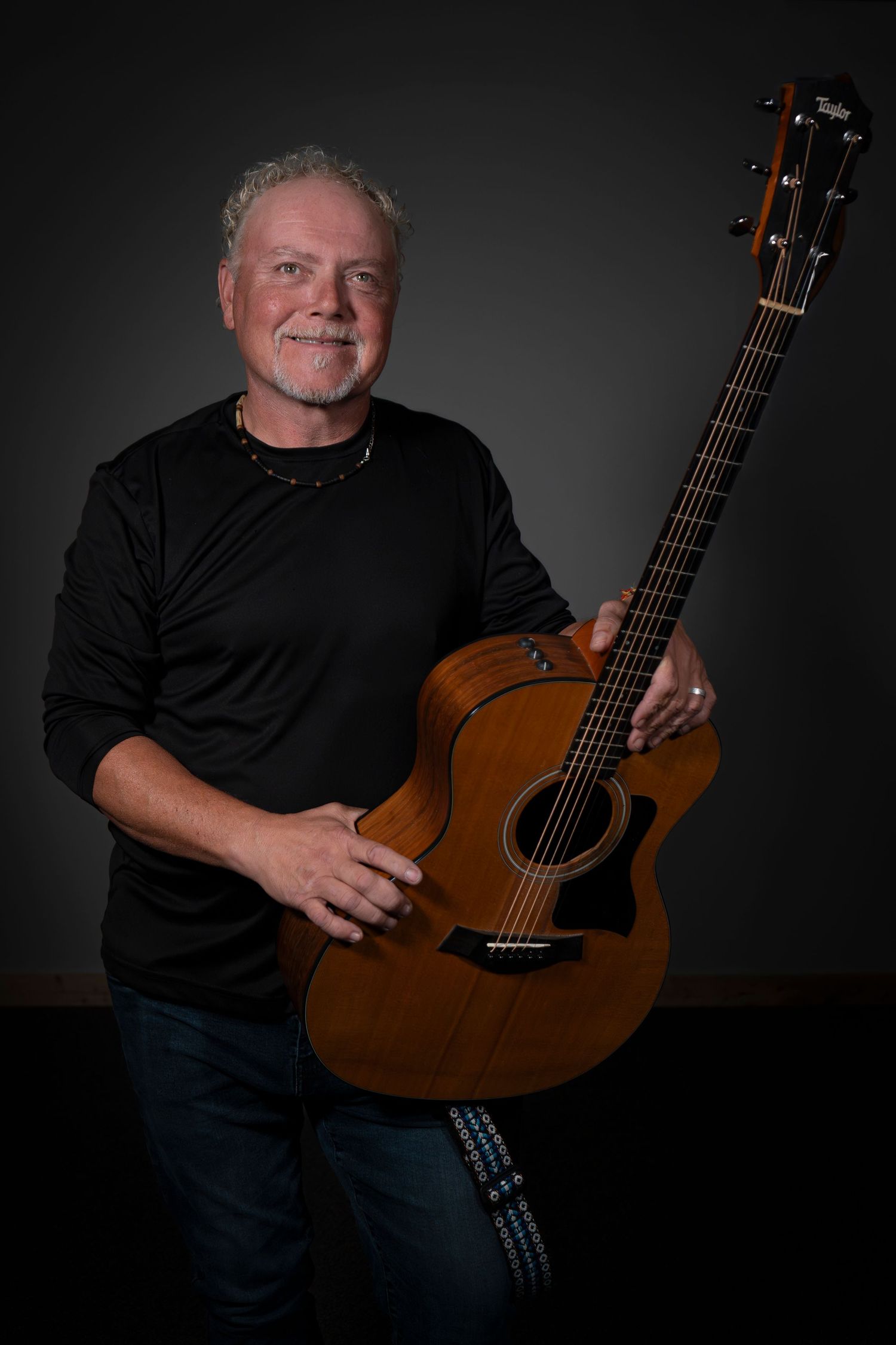 Musician poses with acoustic guitar against dark background in studio portraits.