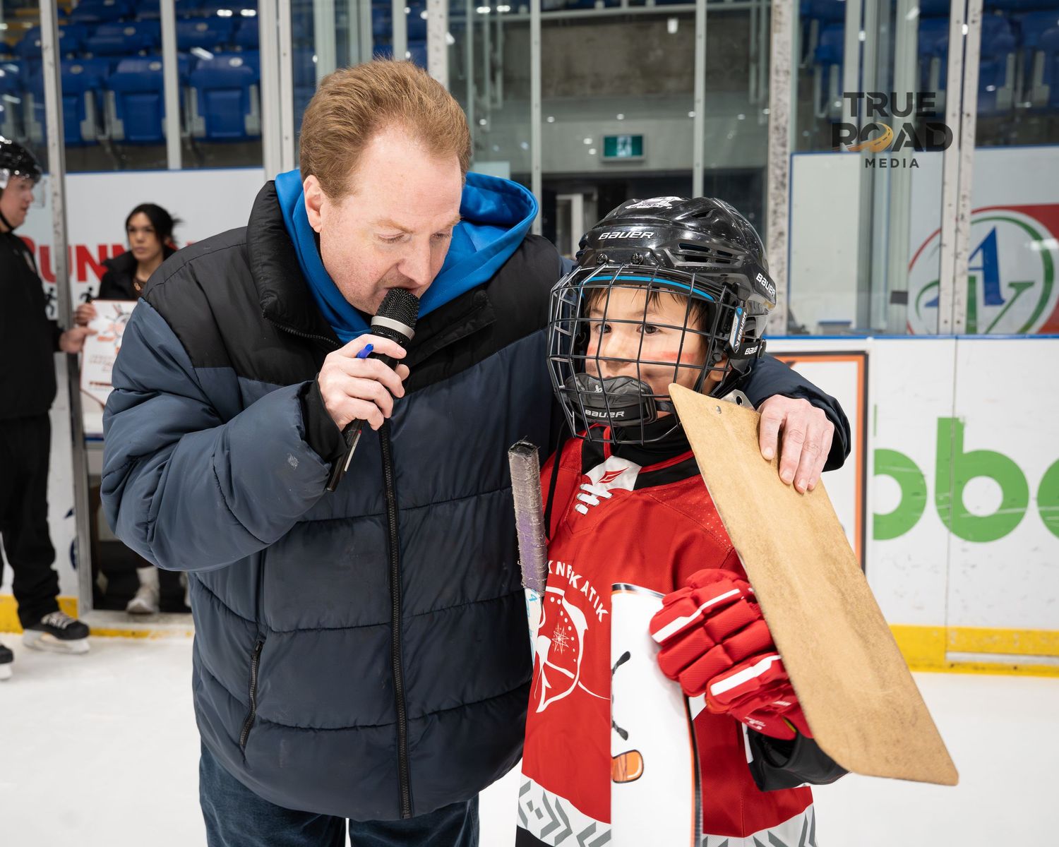 Youth hockey player and adult share a moment near the rink boards during an event.