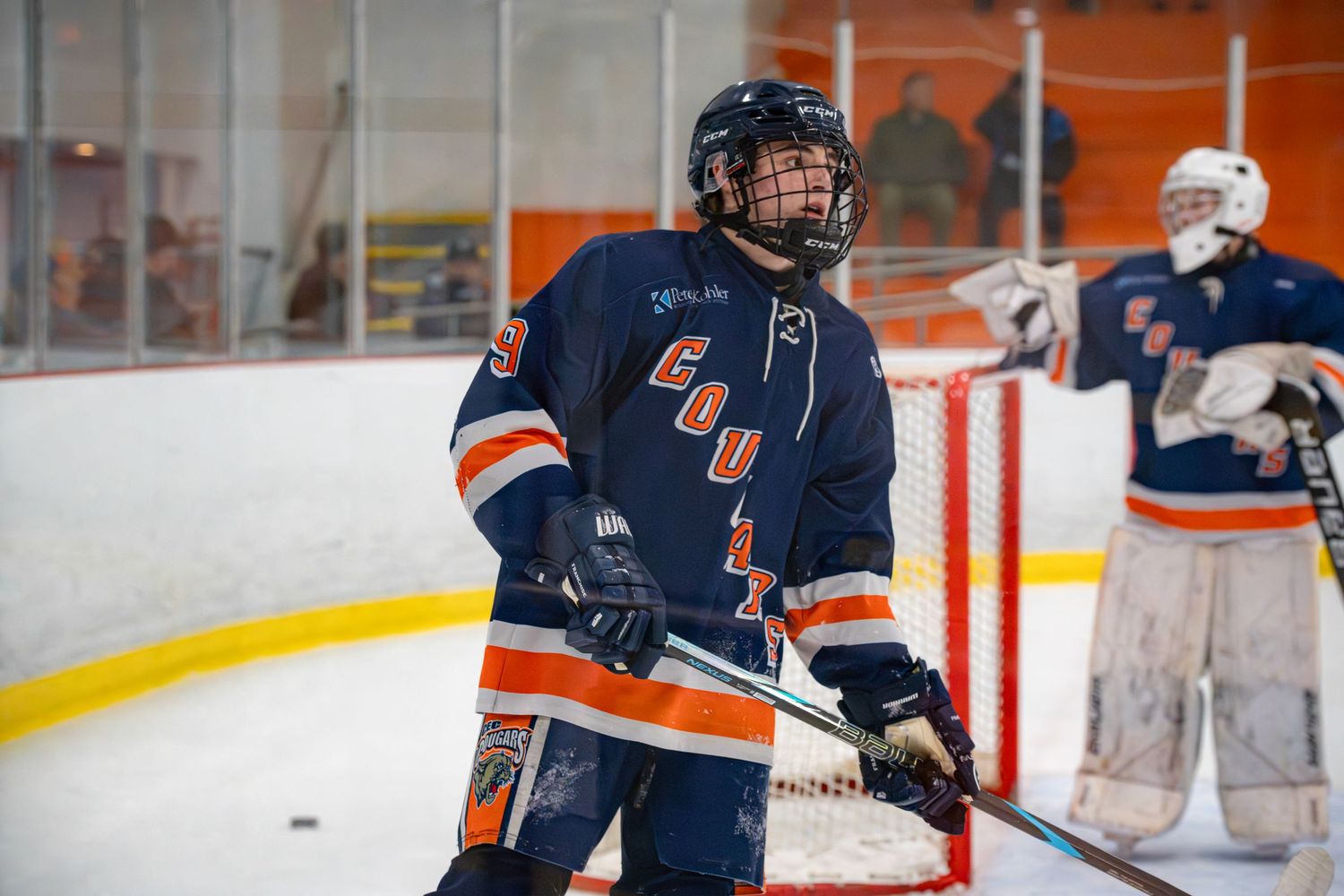 Hockey player in navy and orange jersey takes a shot during an ice hockey game.