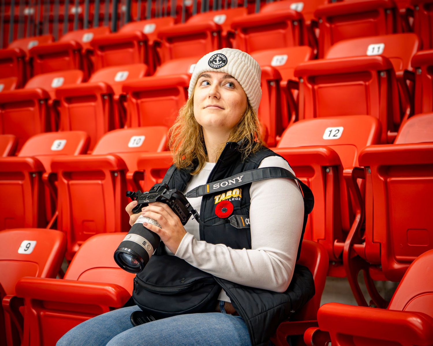 Person in winter clothing sitting alone in arena with red seats.