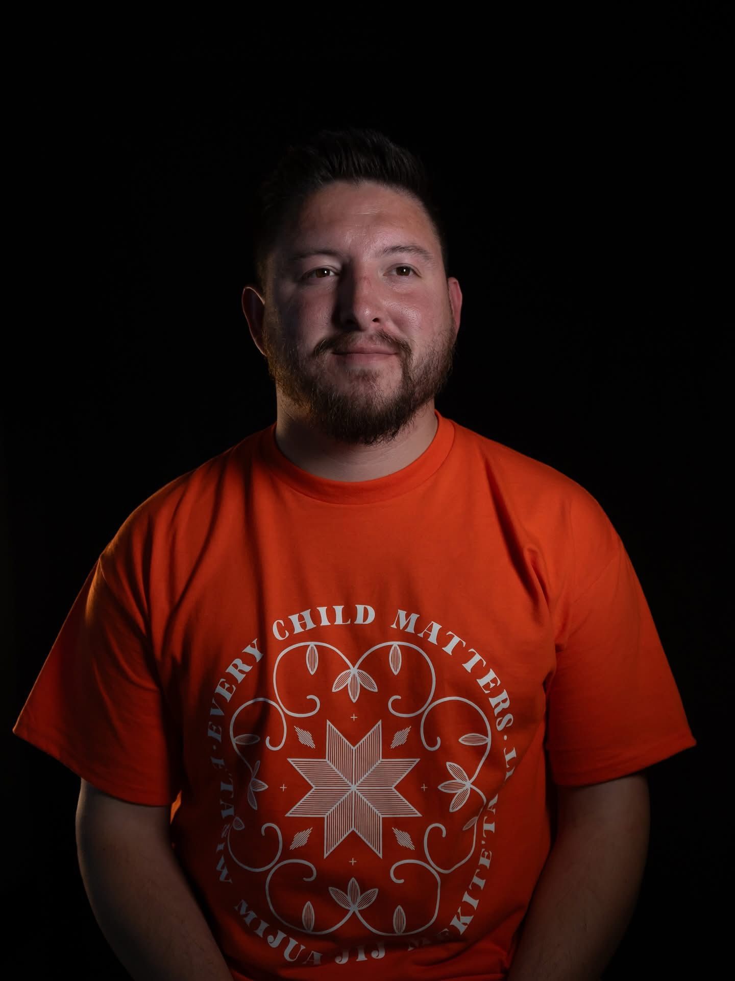 Person in orange t-shirt with decorative star design against black background.