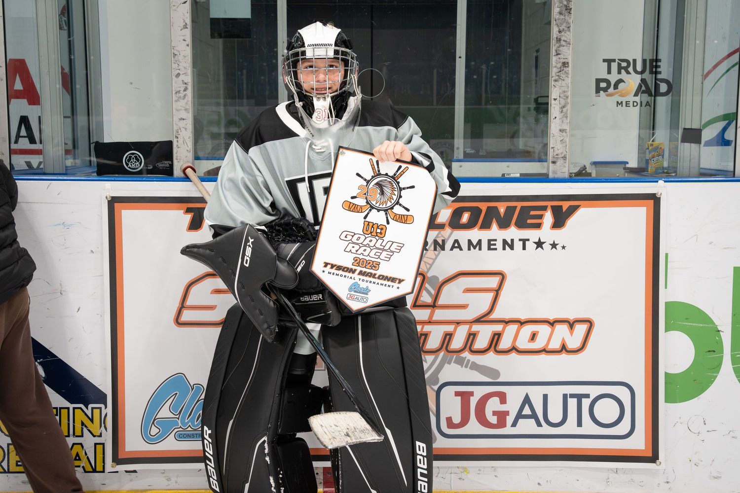 Players gather near the boards of an ice rink with various sponsor advertisements displayed in the background.