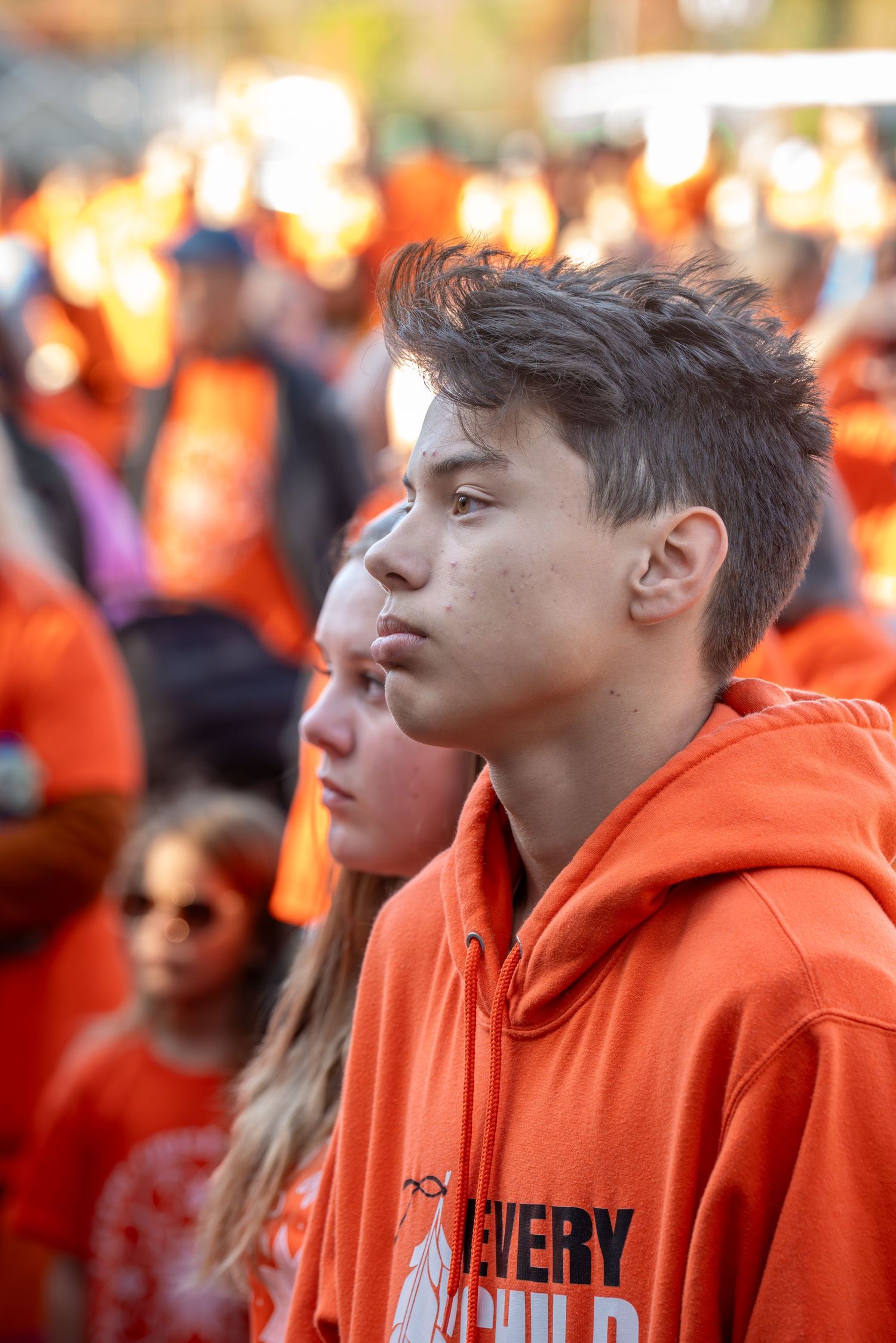 Students in orange hoodies stand together during a school event or rally.