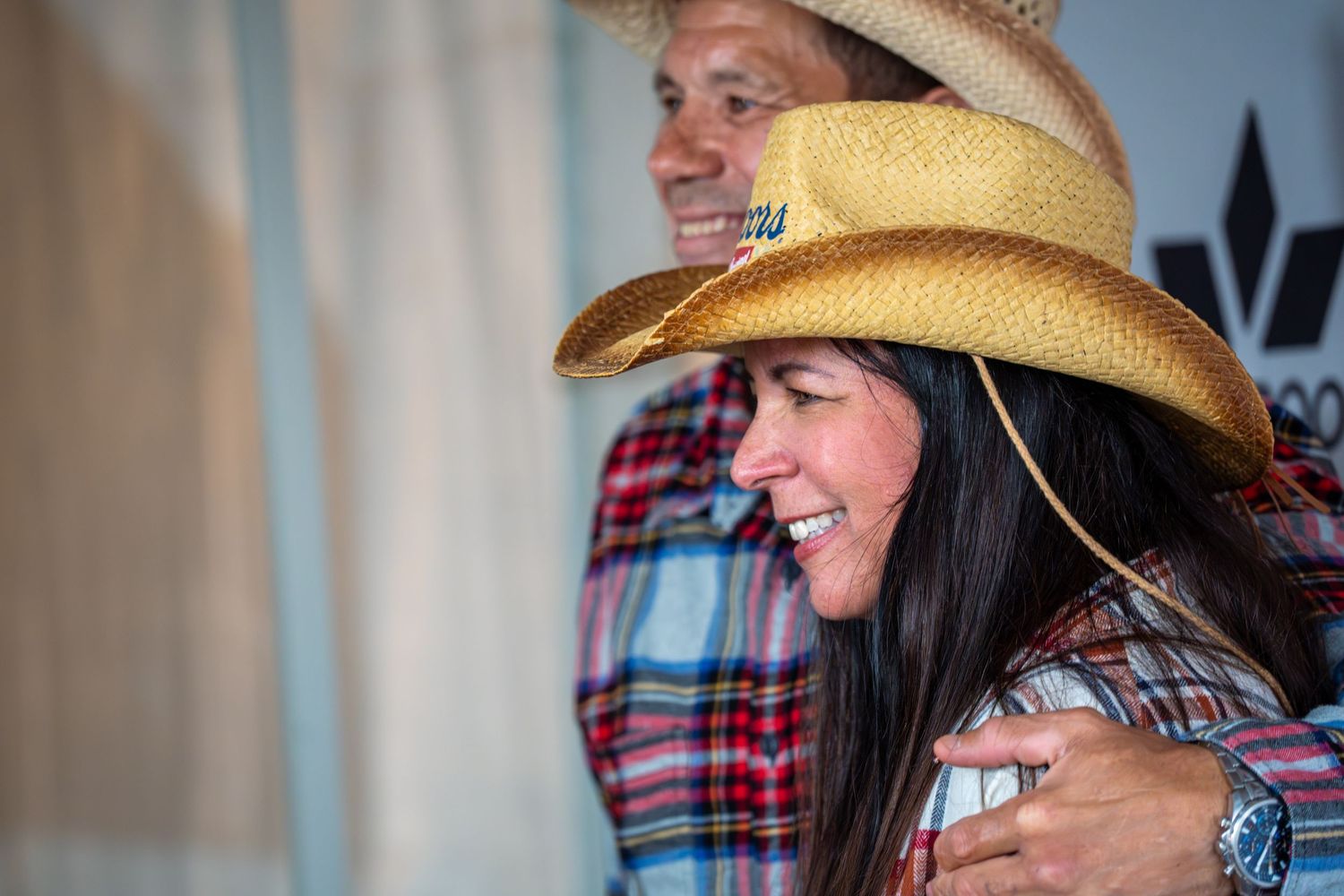 People wearing cowboy hats and plaid shirts smile and laugh together during a casual gathering.