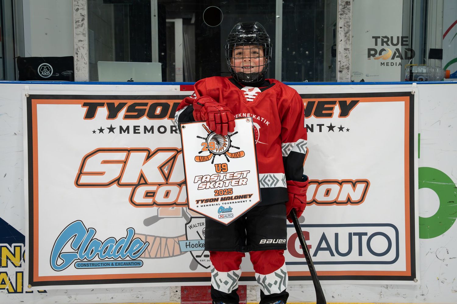 Young hockey player in red jersey poses with tournament award sign.