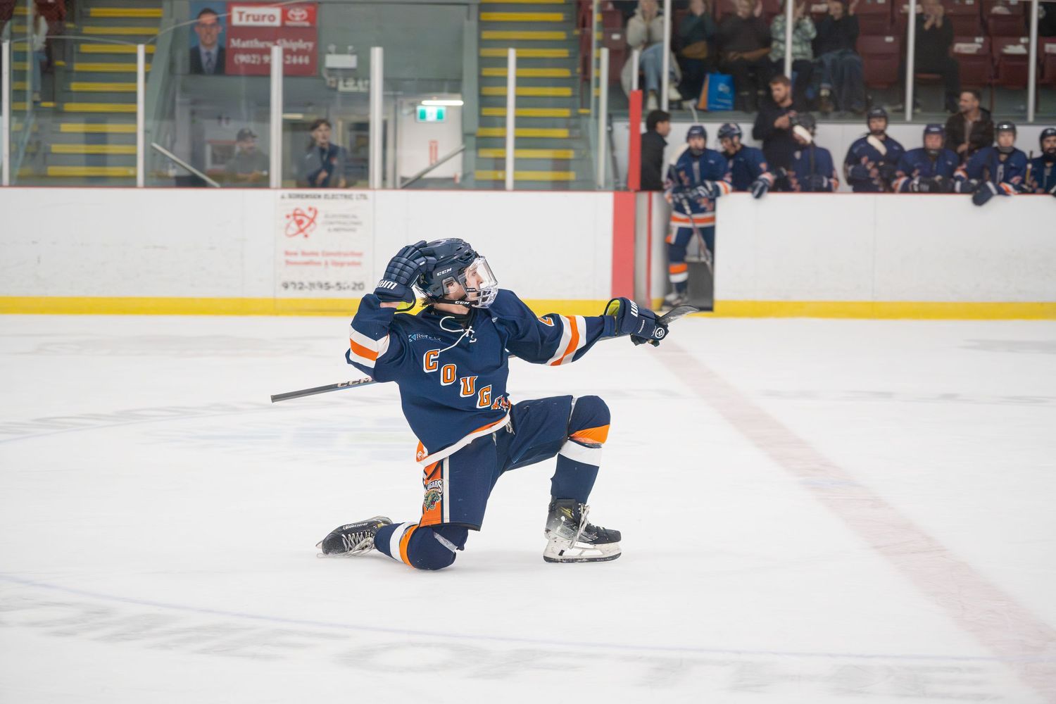 Ice hockey player in blue jersey skates with puck during competitive game action.