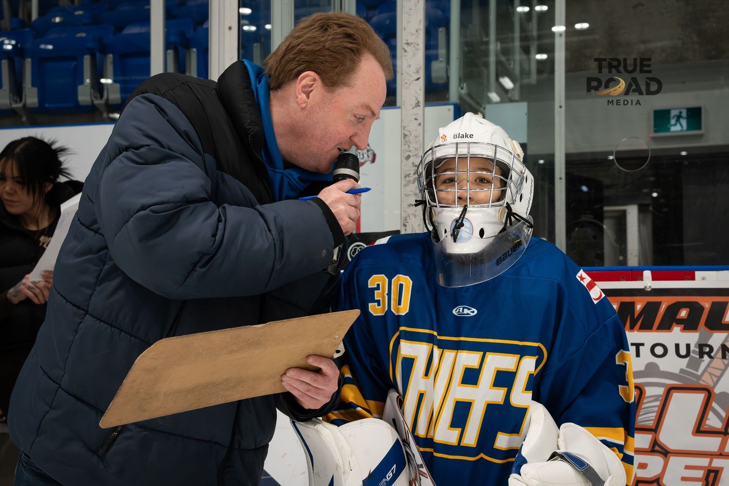 Hockey players and coaches interacting during practice session on the ice rink.