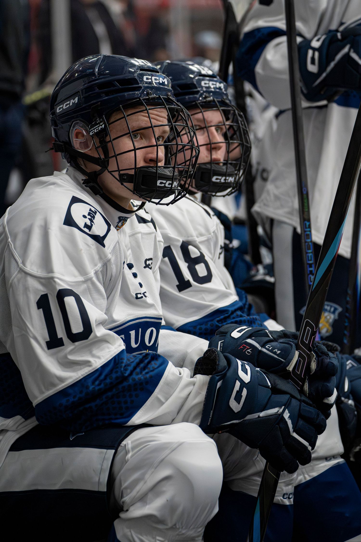 Hockey players in white jerseys and helmets sitting on bench during game.
