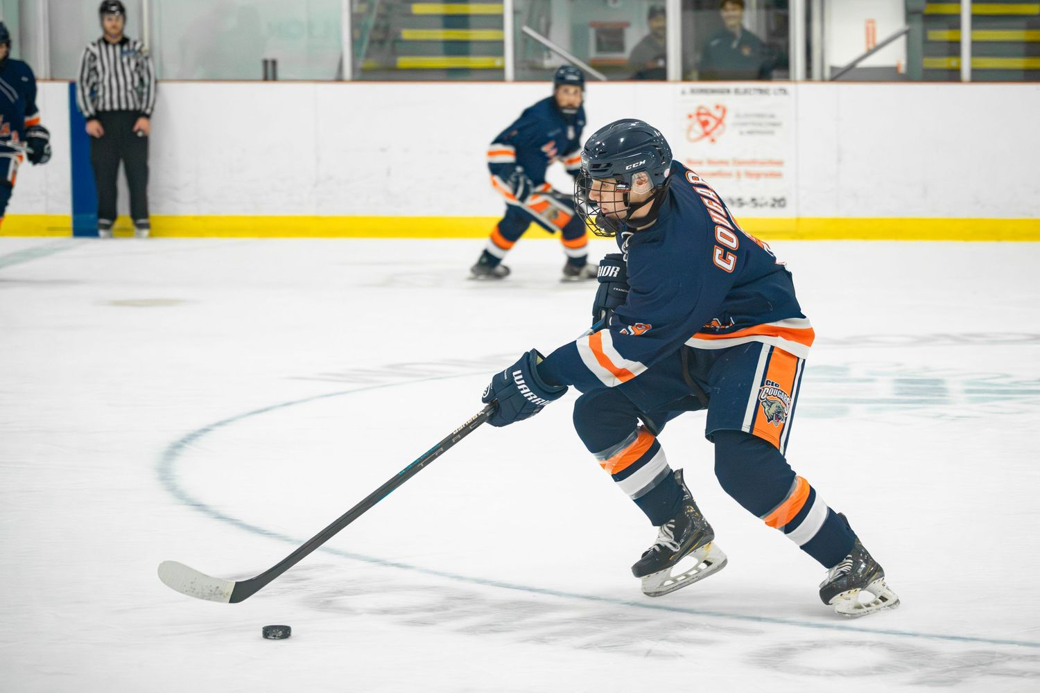 Hockey player in navy and orange uniform controls puck on ice rink during game.