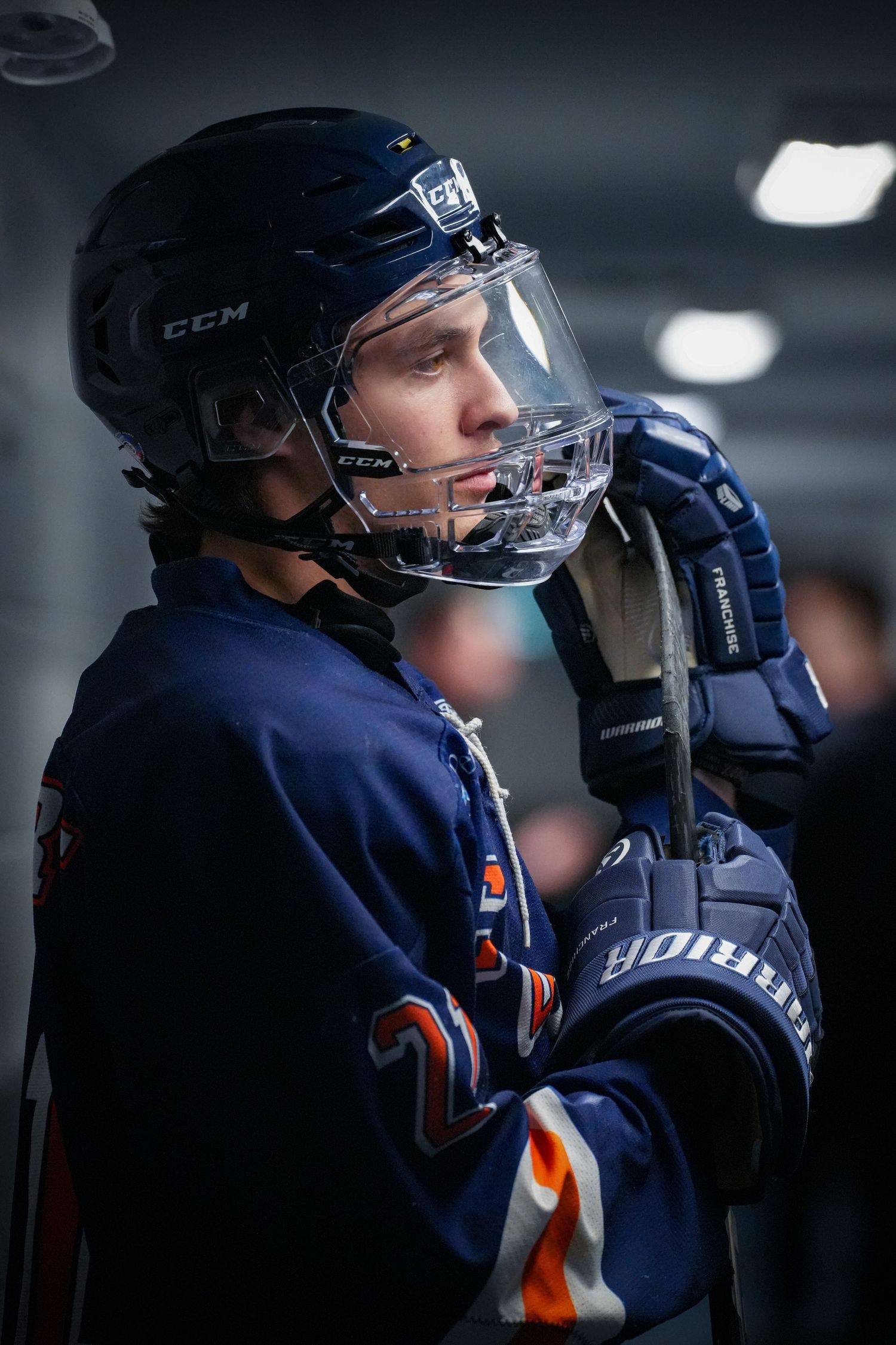 Hockey player in navy blue uniform and CCM helmet adjusts their face shield during a game.