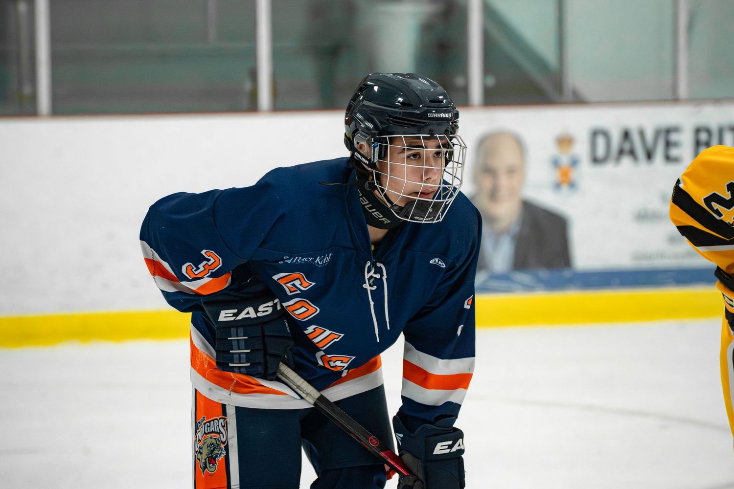 Ice hockey player in navy blue jersey skates with stick during competitive match.
