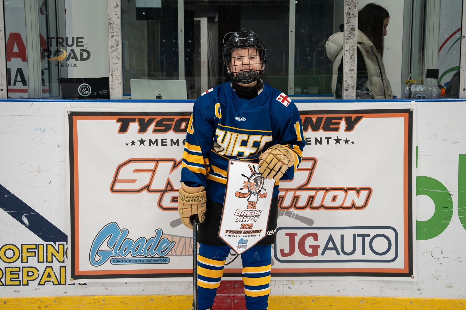 Hockey players in blue and white jerseys stand near the boards during a game with arena advertising visible.