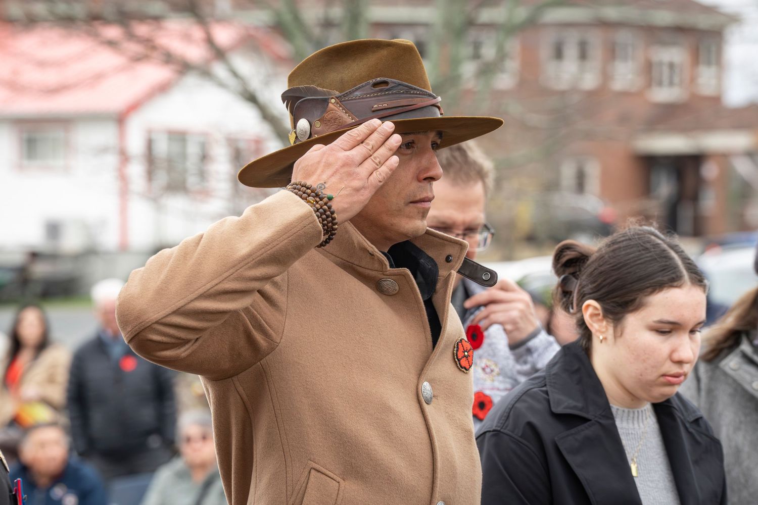 People wearing brown coats and hats gather at an outdoor event on an overcast day.
