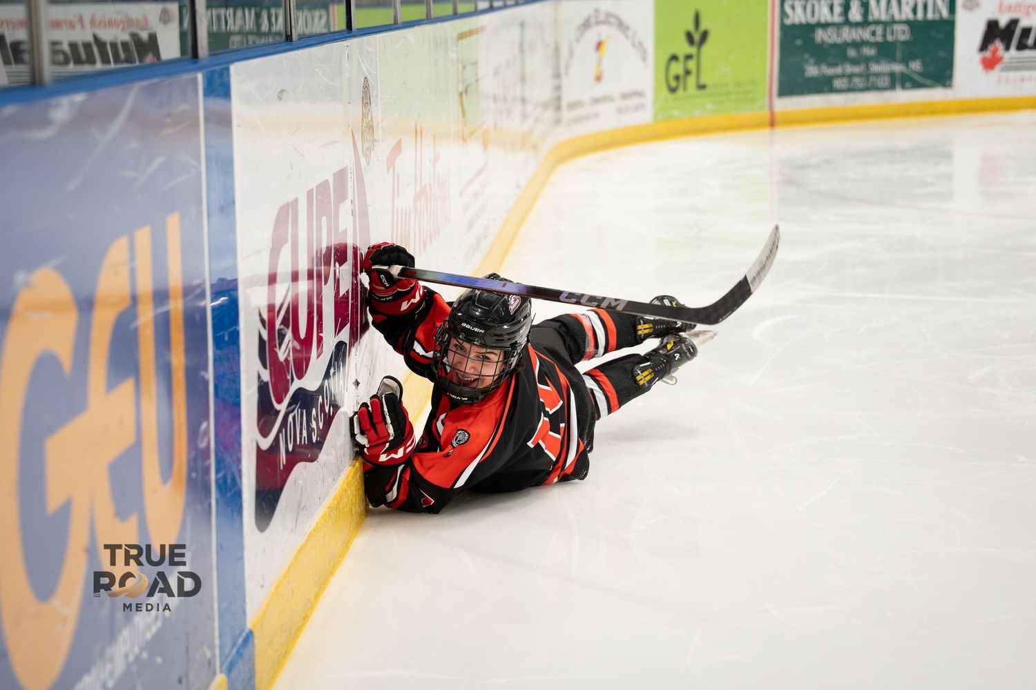 Hockey player in red jersey slides across ice during intense game action.