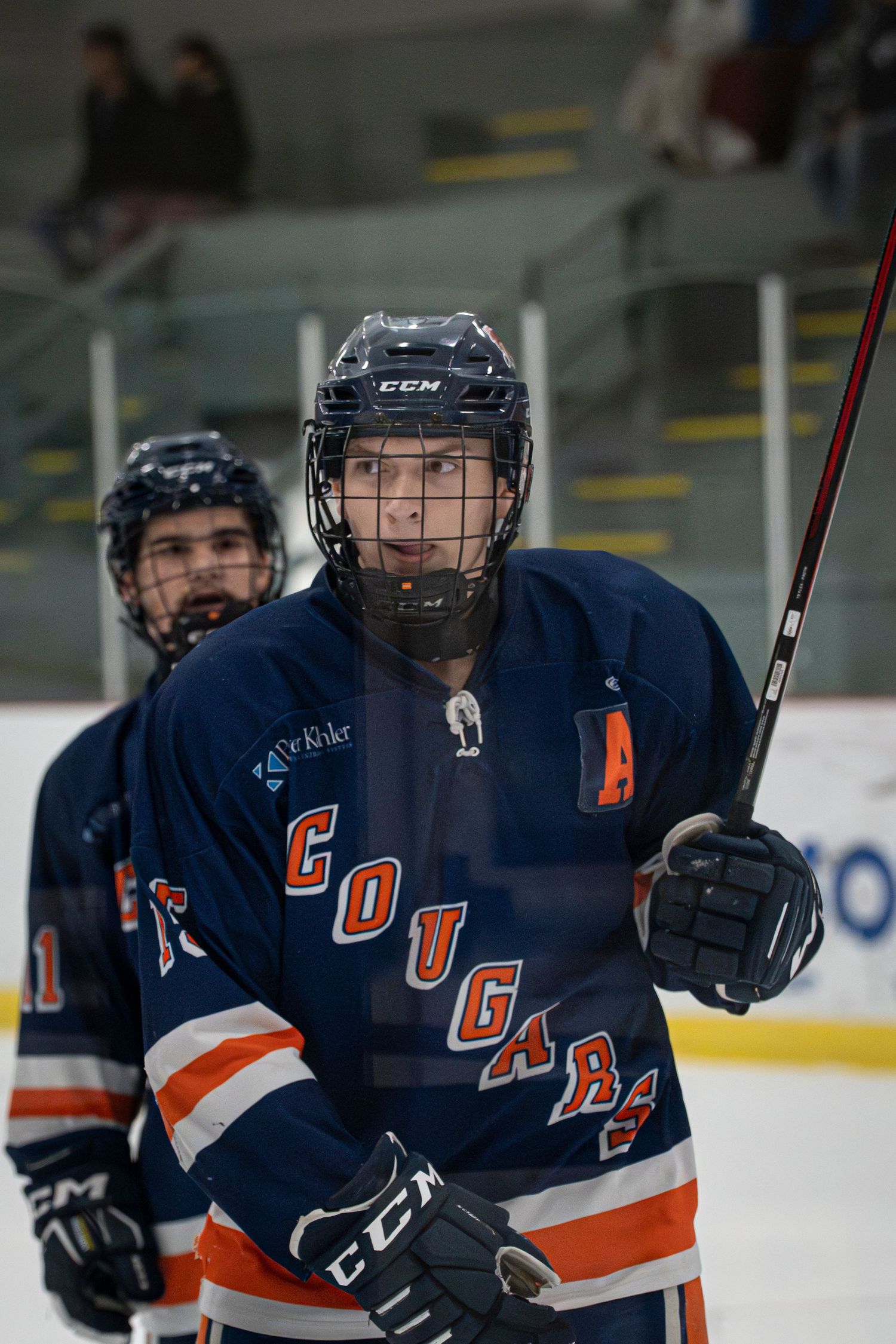 Hockey players in navy blue and orange jerseys skate on ice during a game.