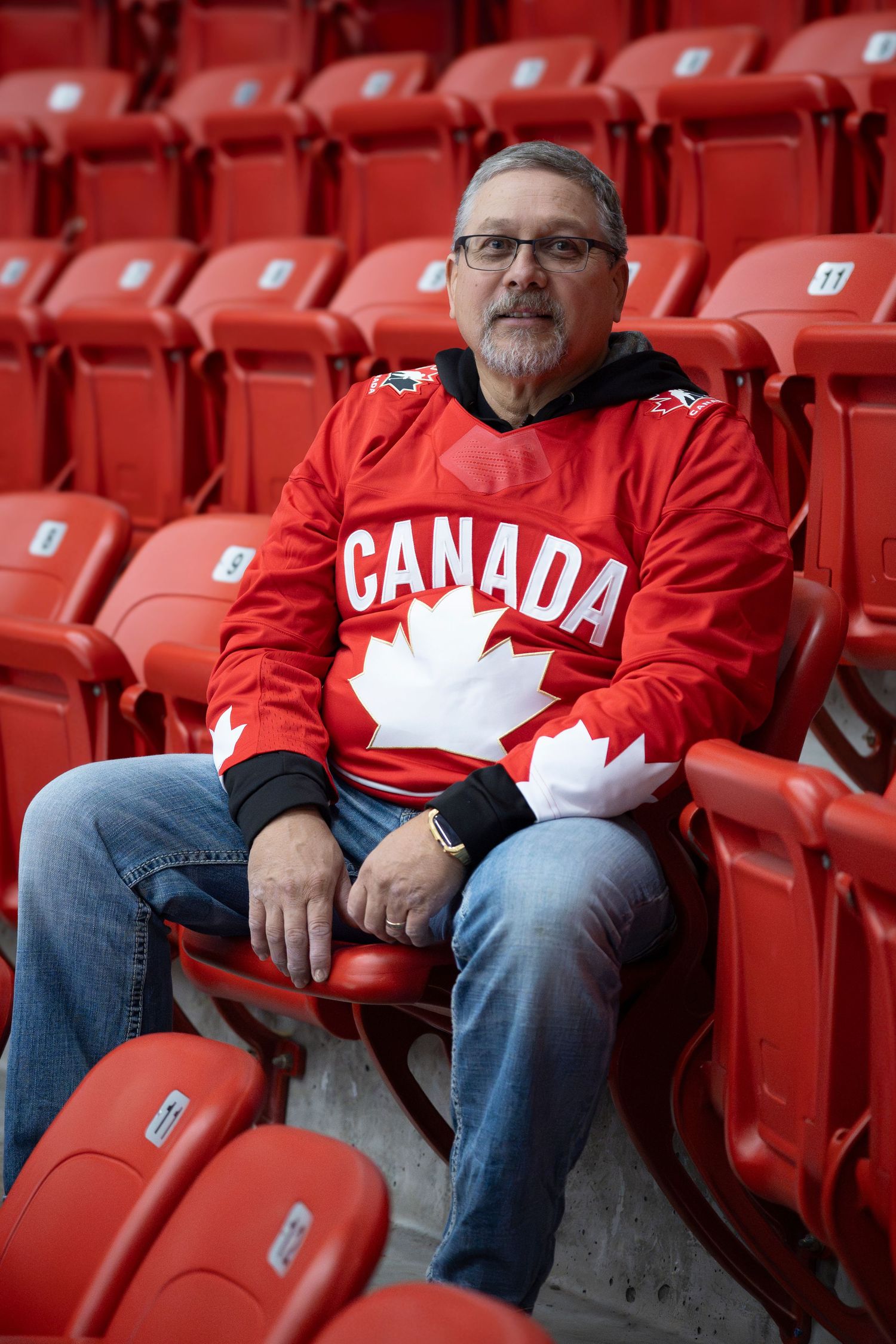 Person wearing Canada hockey jersey sitting in red stadium seats.
