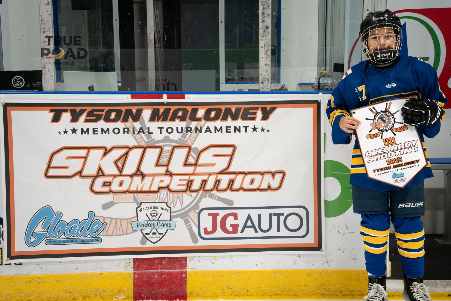 Young hockey player in blue uniform poses with skills competition banner and award.