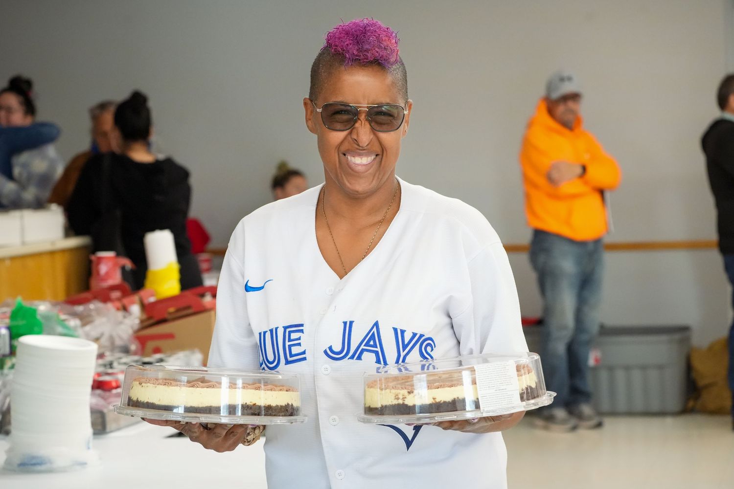 Volunteers serve food at a community meal event with smiling faces and blue shirts.