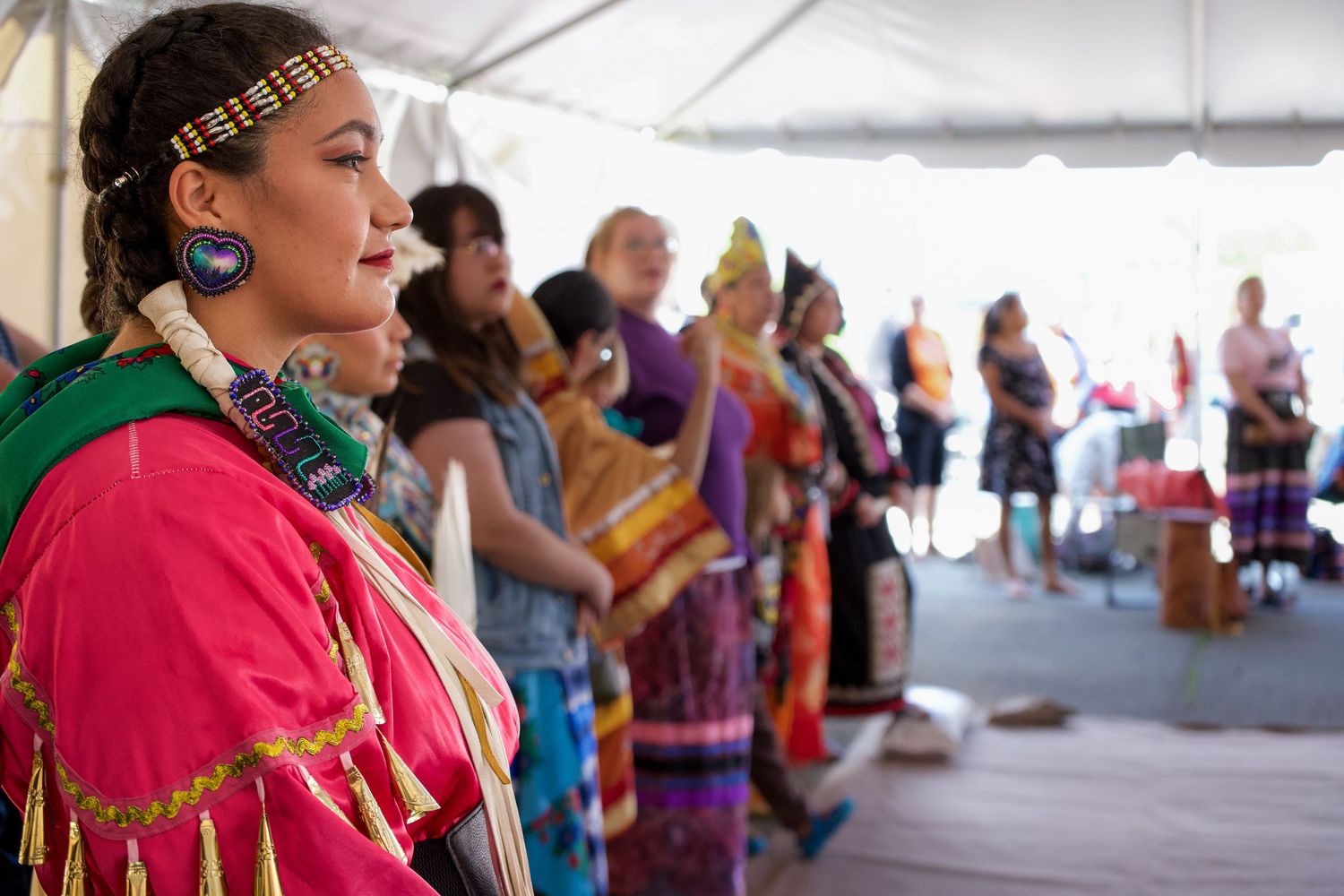Colorfully dressed performers entertain audience under large white tent.