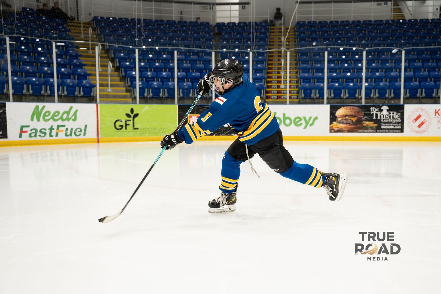 Hockey player in blue jersey practices skating with puck on indoor ice rink.