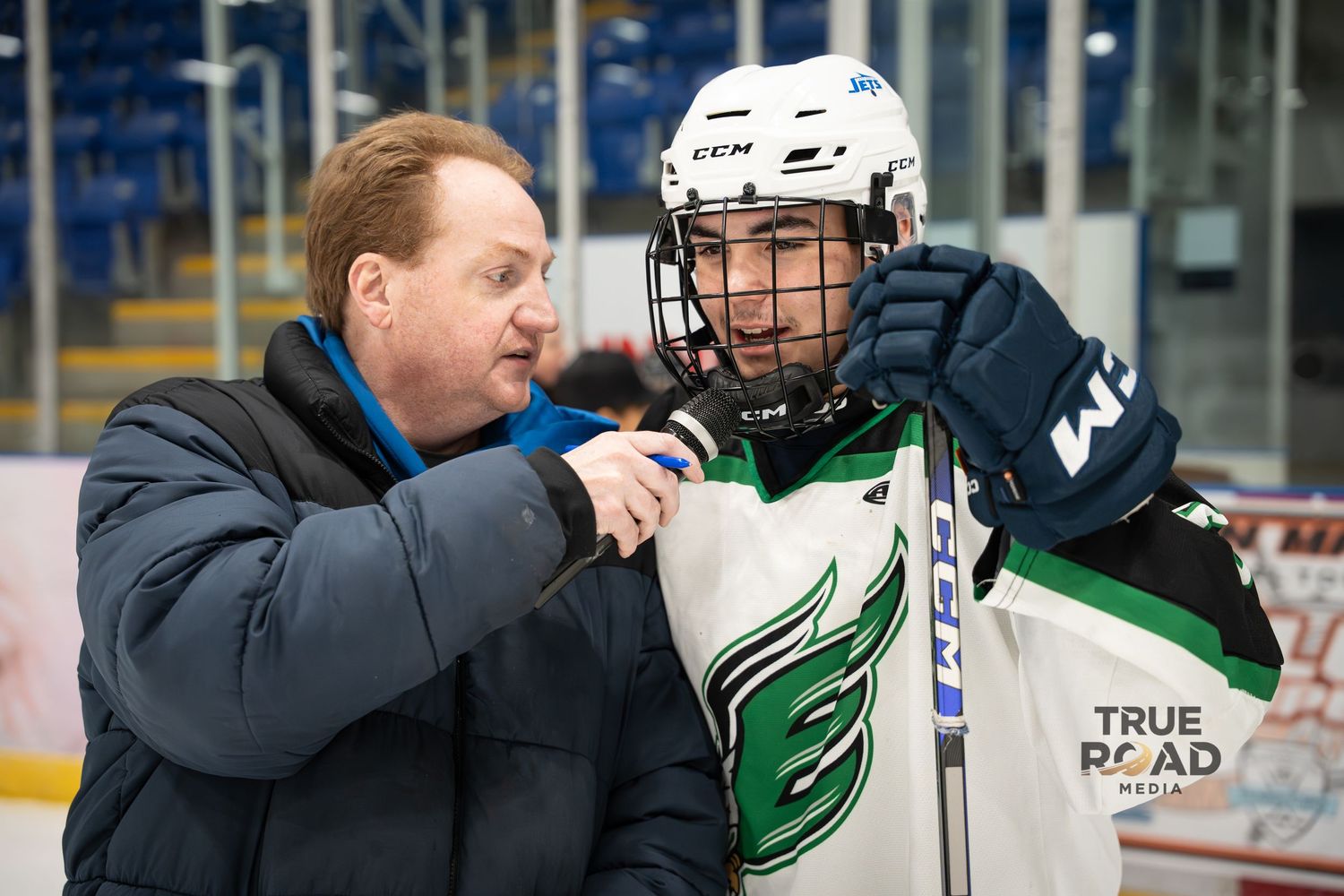 Sports reporter interviews hockey player wearing green jersey and helmet during game coverage.
