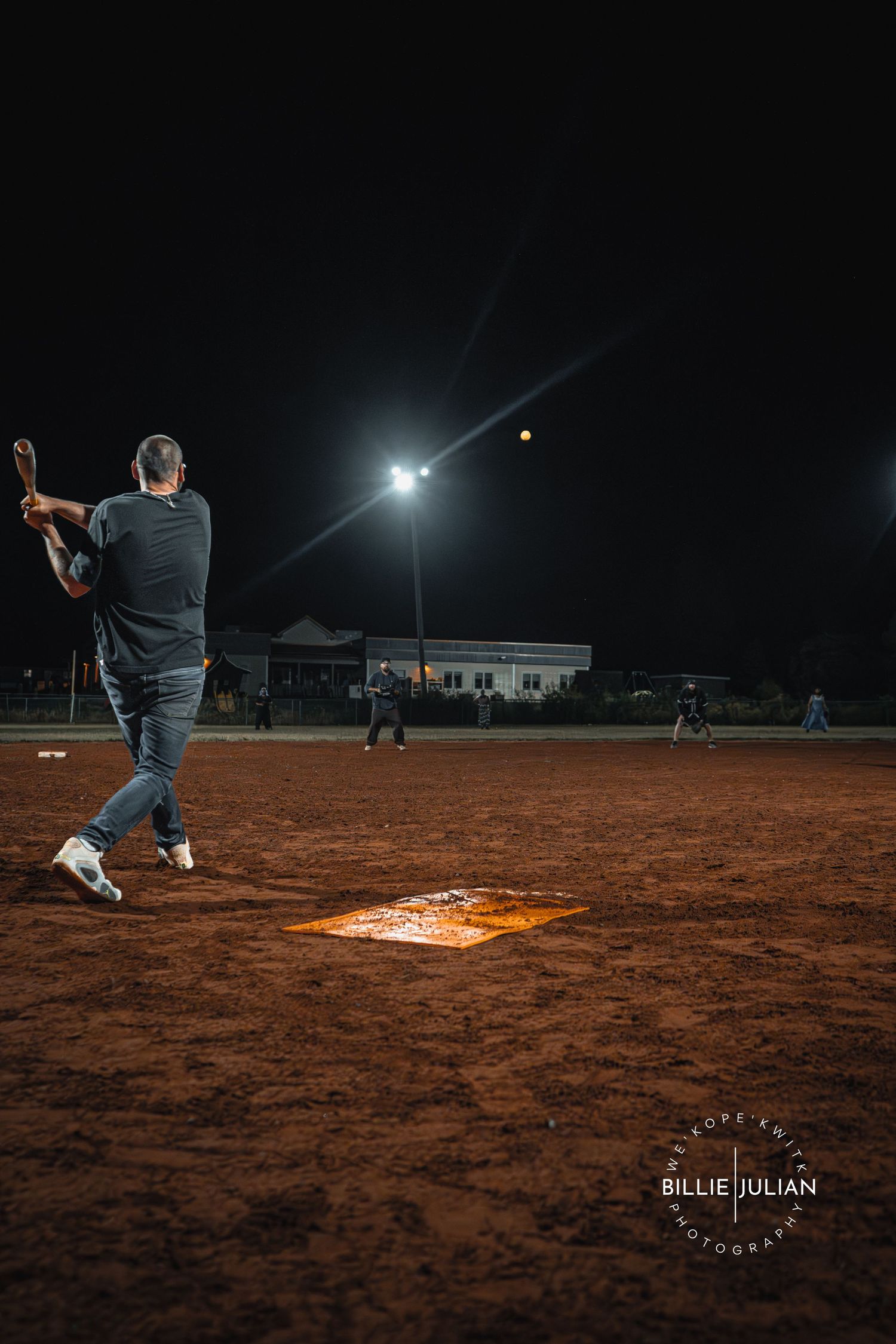 Player approaching illuminated base during nighttime softball game on dirt field.