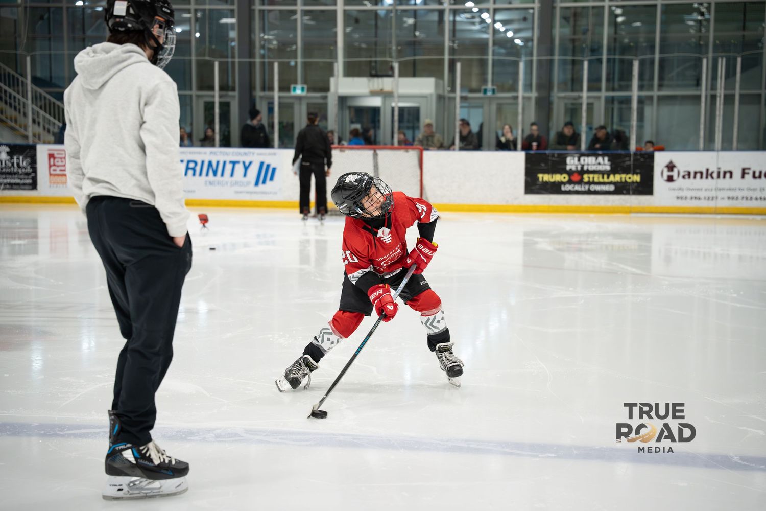 Hockey players practice skating drills on an indoor ice rink with advertising boards visible along the sides.