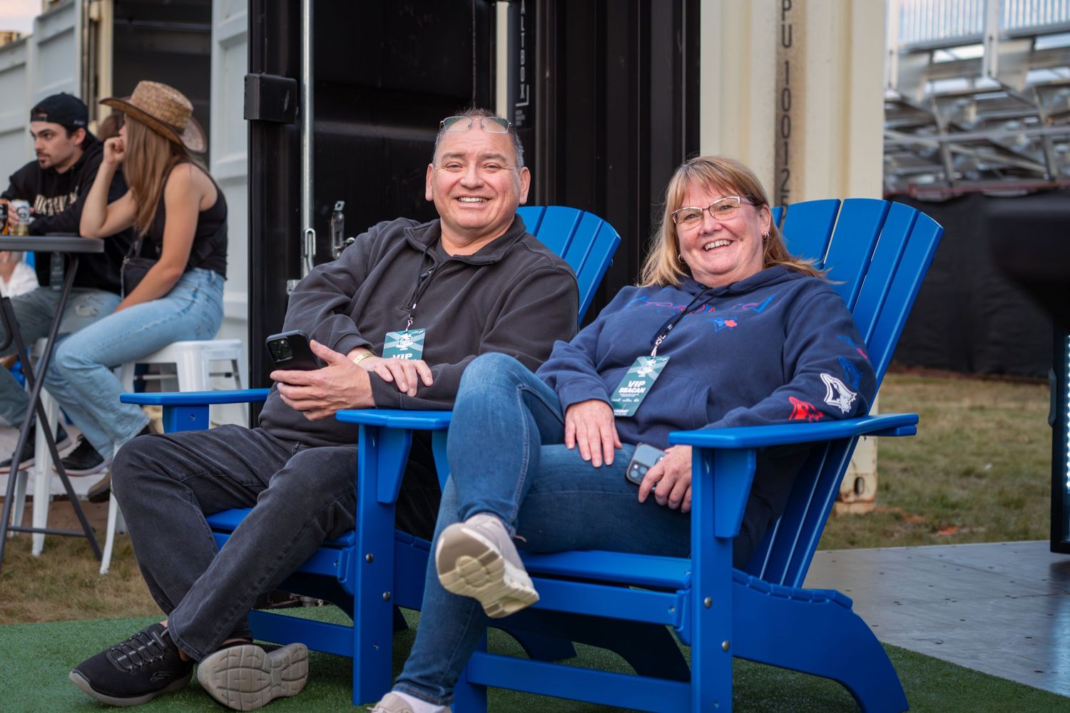 People relaxing in bright blue Adirondack chairs on an outdoor patio during a gathering.