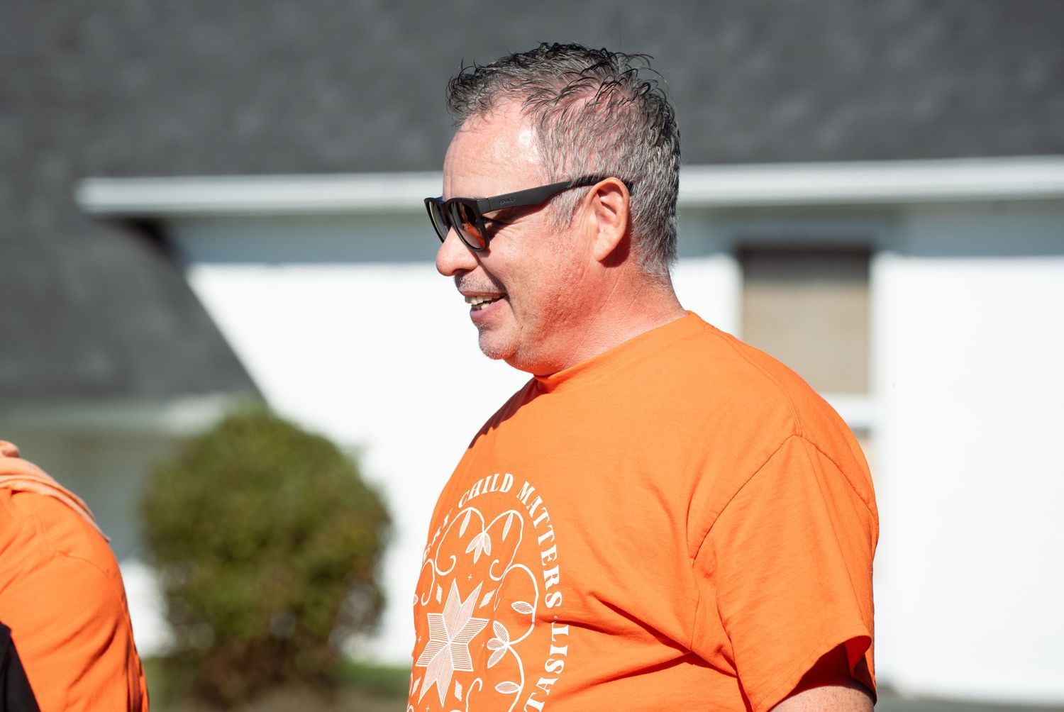 People in orange shirts with a logo design standing outdoors on a sunny day.