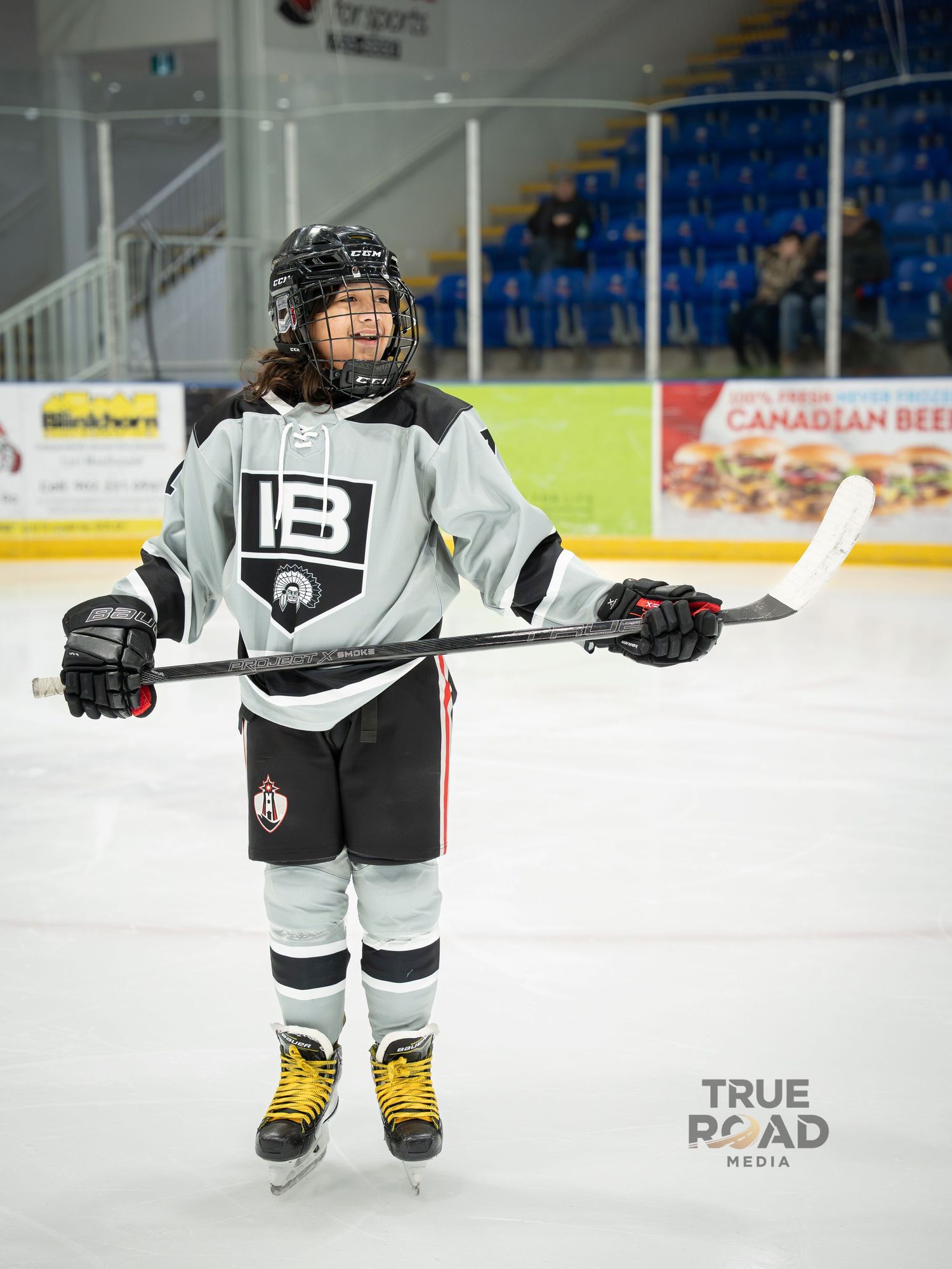 Hockey player in white jersey and helmet skating on ice rink with advertising boards visible in background.