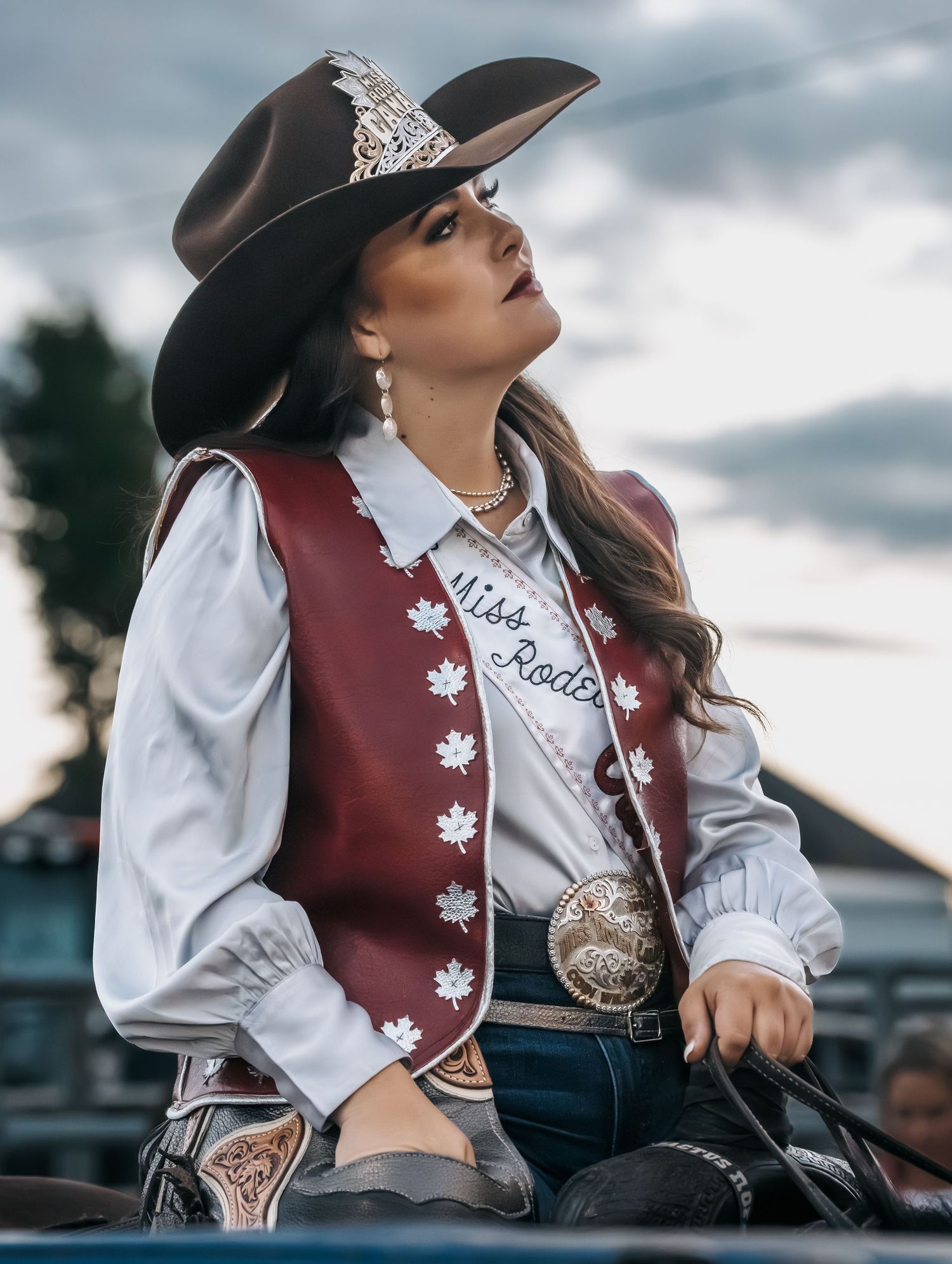 Traditional western attire featuring a burgundy vest with maple leaf details against a dramatic cloudy sky.