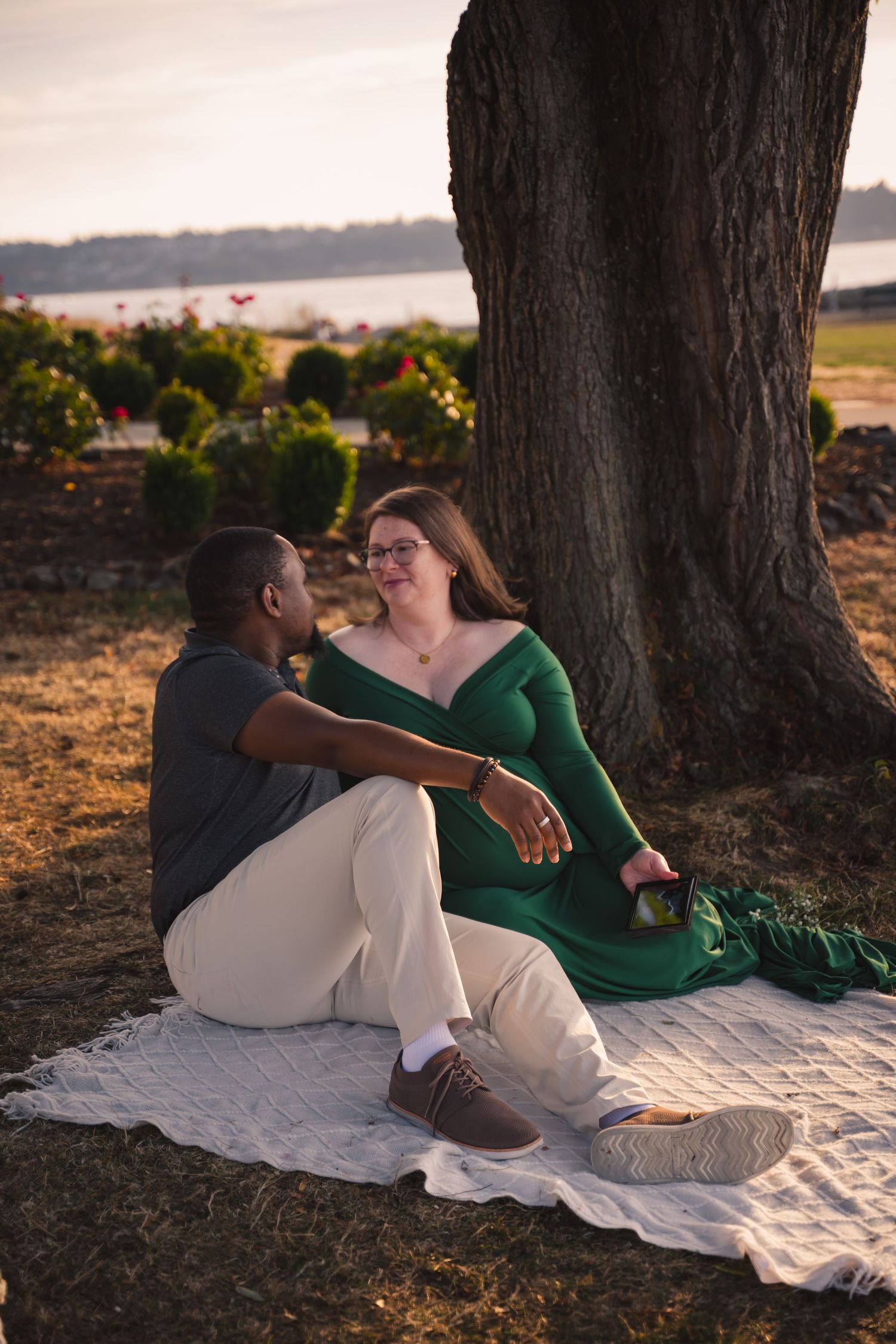 A couple relaxes together on a white blanket under a tree during golden hour sunset.