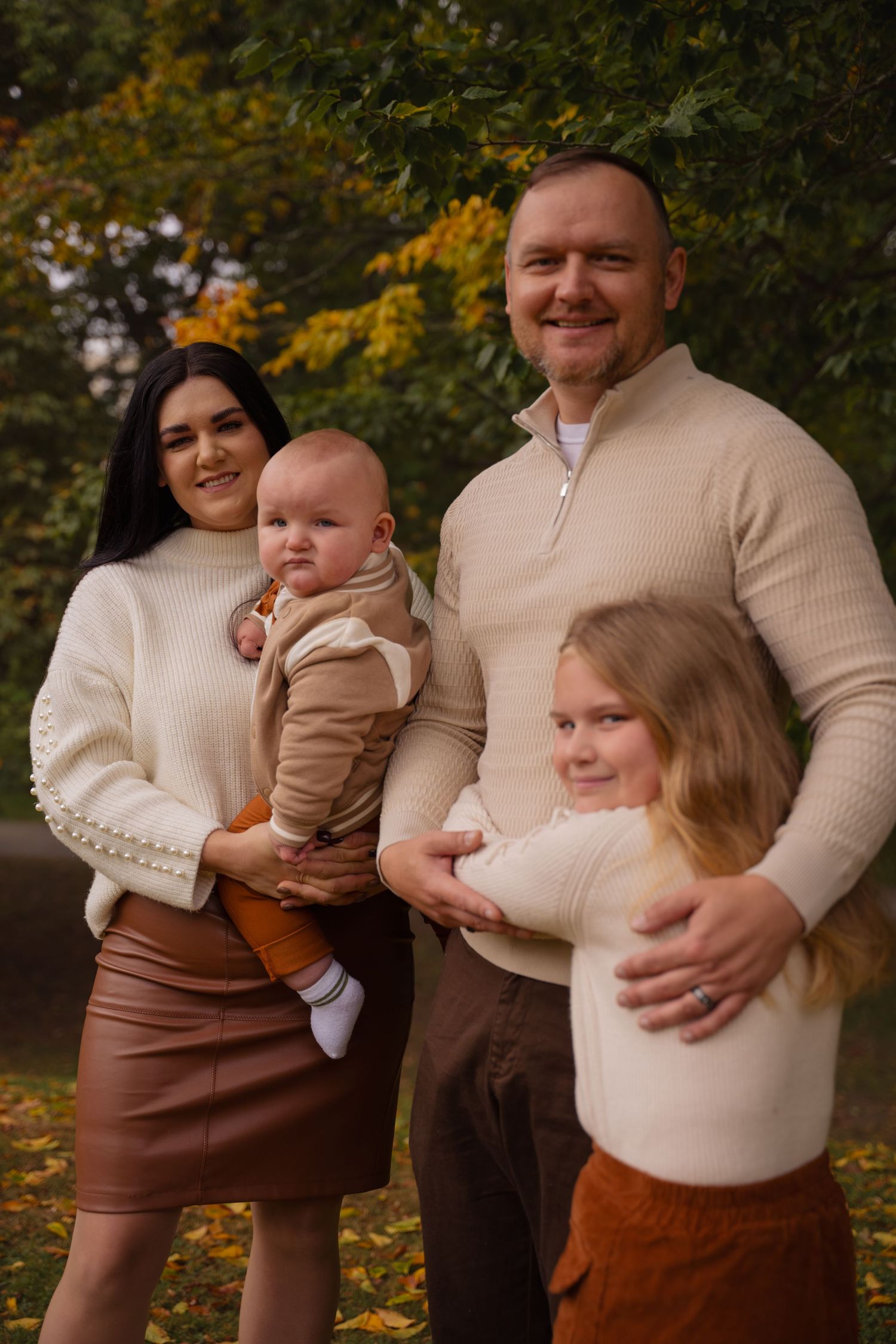 A family wearing coordinated cream and brown outfits poses together during an autumn outdoor photo session.