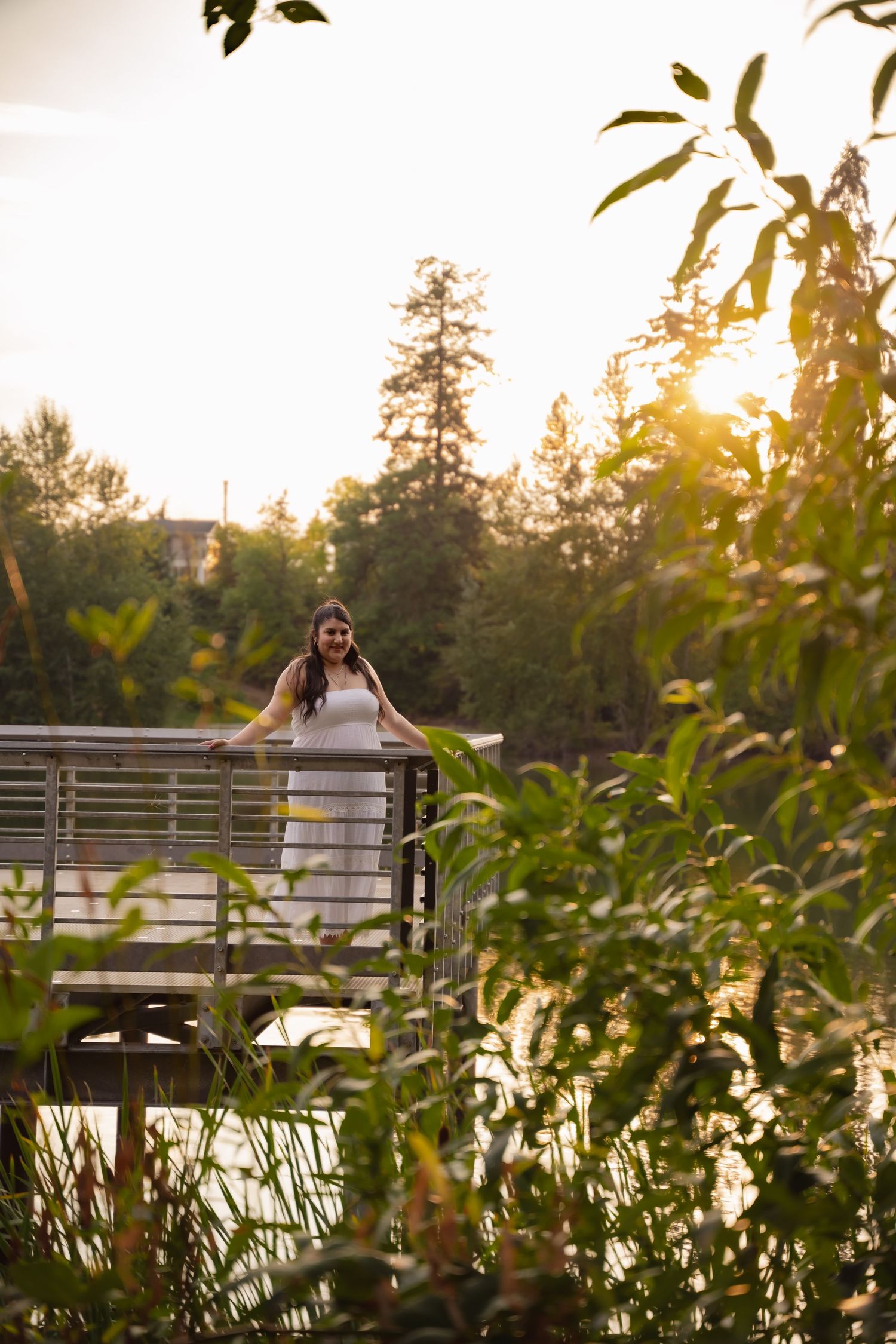 Bride in white dress sits peacefully on wooden bench at sunset surrounded by lush greenery in outdoor garden setting.